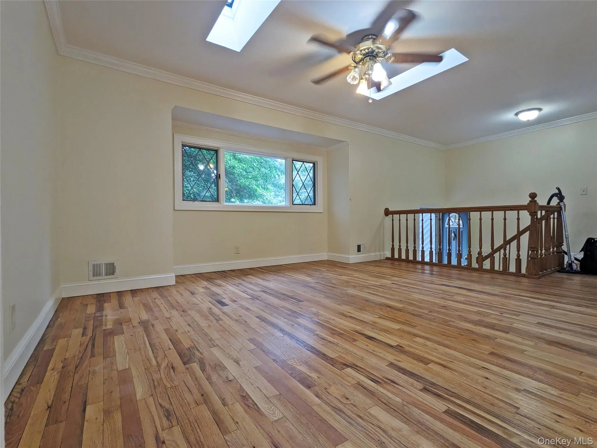 Spacious room featuring wood-finish flooring, a decorative ceiling fan, and two skylights for natural illumination Spacious room featuring wood-finish flooring, a decorative ceiling fan, and two skylights for natural illumination