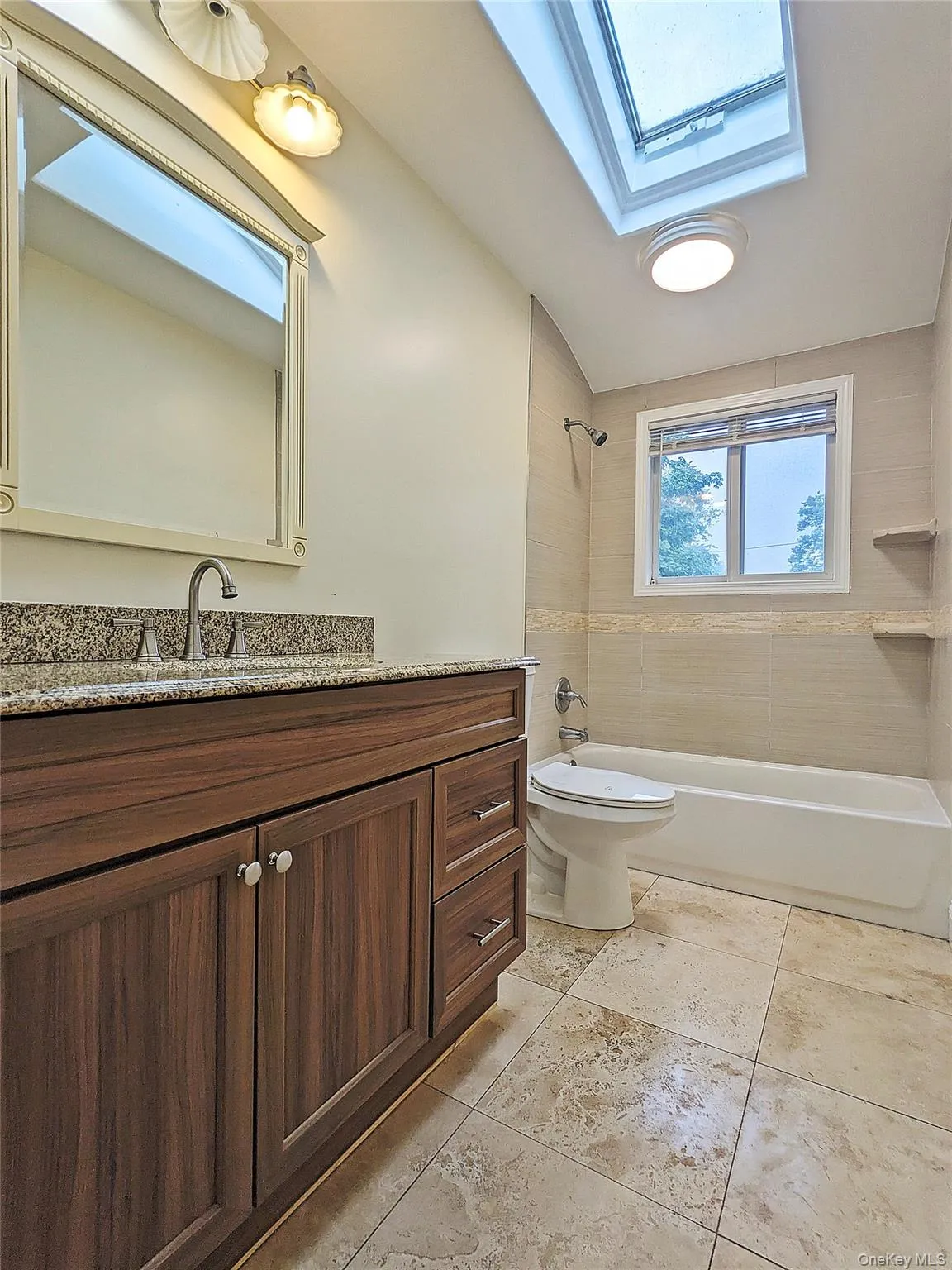 Bathroom featuring a wood-finish vanity with a speckled countertop, a skylight, a built-in bathtub, and tiled flooring Bathroom featuring a wood-finish vanity with a speckled countertop, a skylight, a built-in bathtub, and tiled flooring