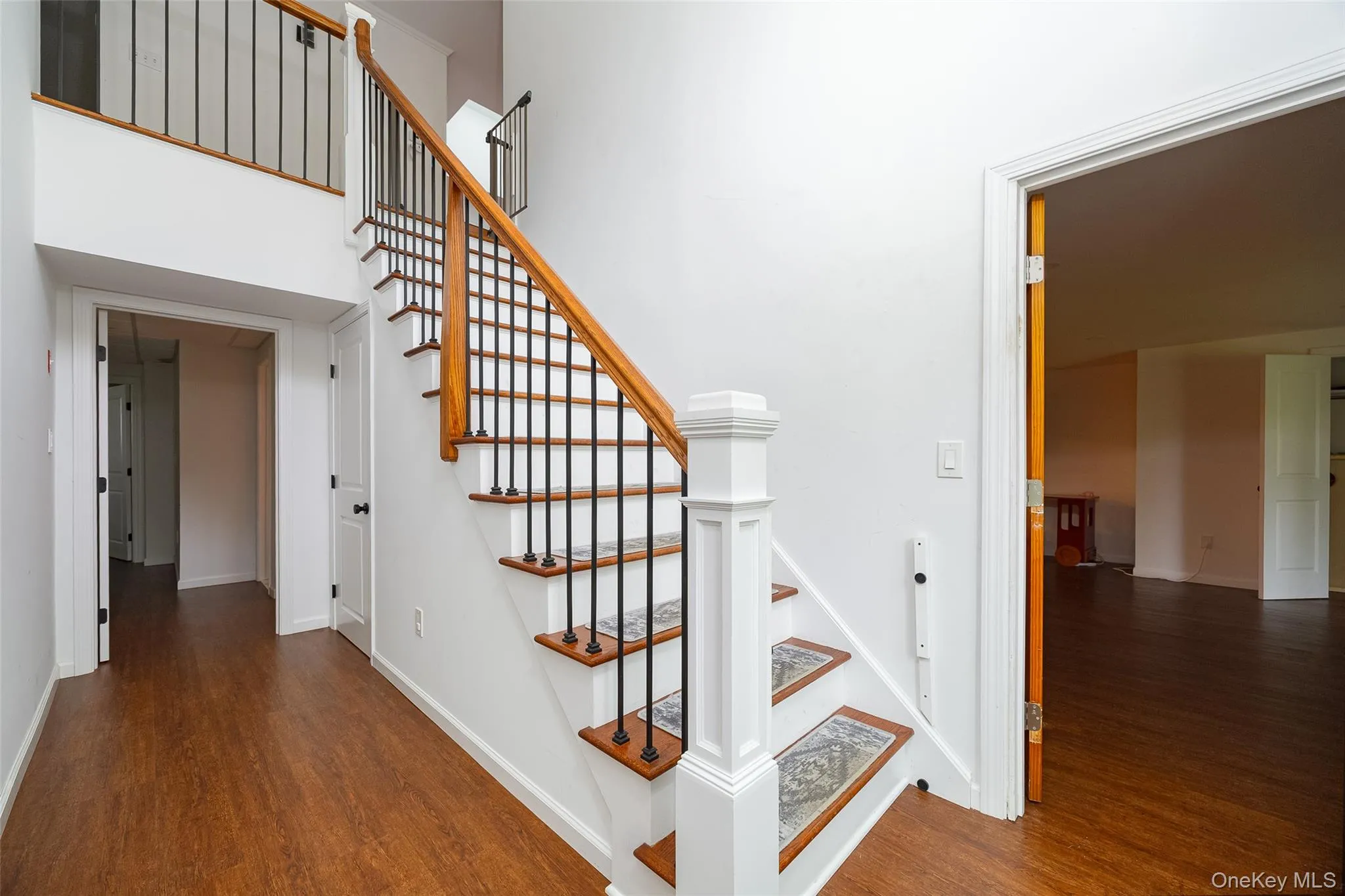 Lower level entryway featuring wood-finish flooring, a staircase with wood treads and a wrought iron baluster system, and white trim Lower level entryway featuring wood-finish flooring, a staircase with wood treads and a wrought iron baluster system, and white trim