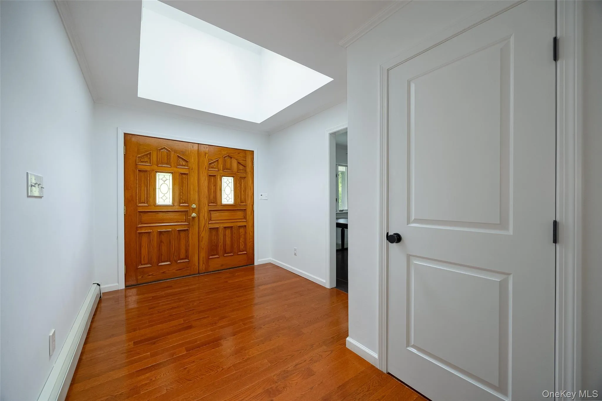 Entryway featuring double wood entry doors with decorative glass panels, wood-finish flooring, a skylight, and white walls Entryway featuring double wood entry doors with decorative glass panels, wood-finish flooring, a skylight, and white walls
