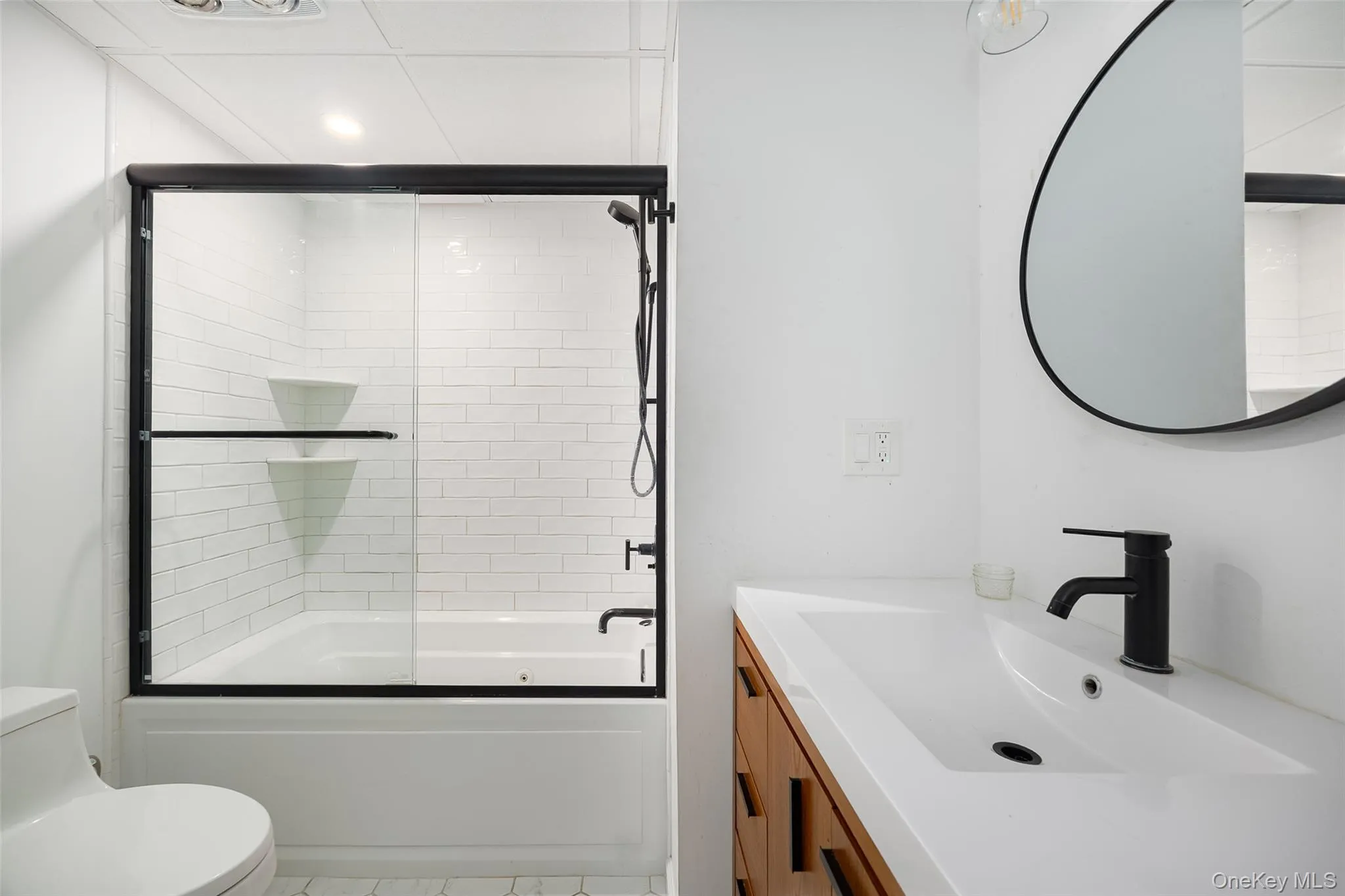 Bathroom featuring a white subway tile shower surround with black-framed glass sliding doors, a matching black shower head, and built-in shelving Bathroom featuring a white subway tile shower surround with black-framed glass sliding doors, a matching black shower head, and built-in shelving