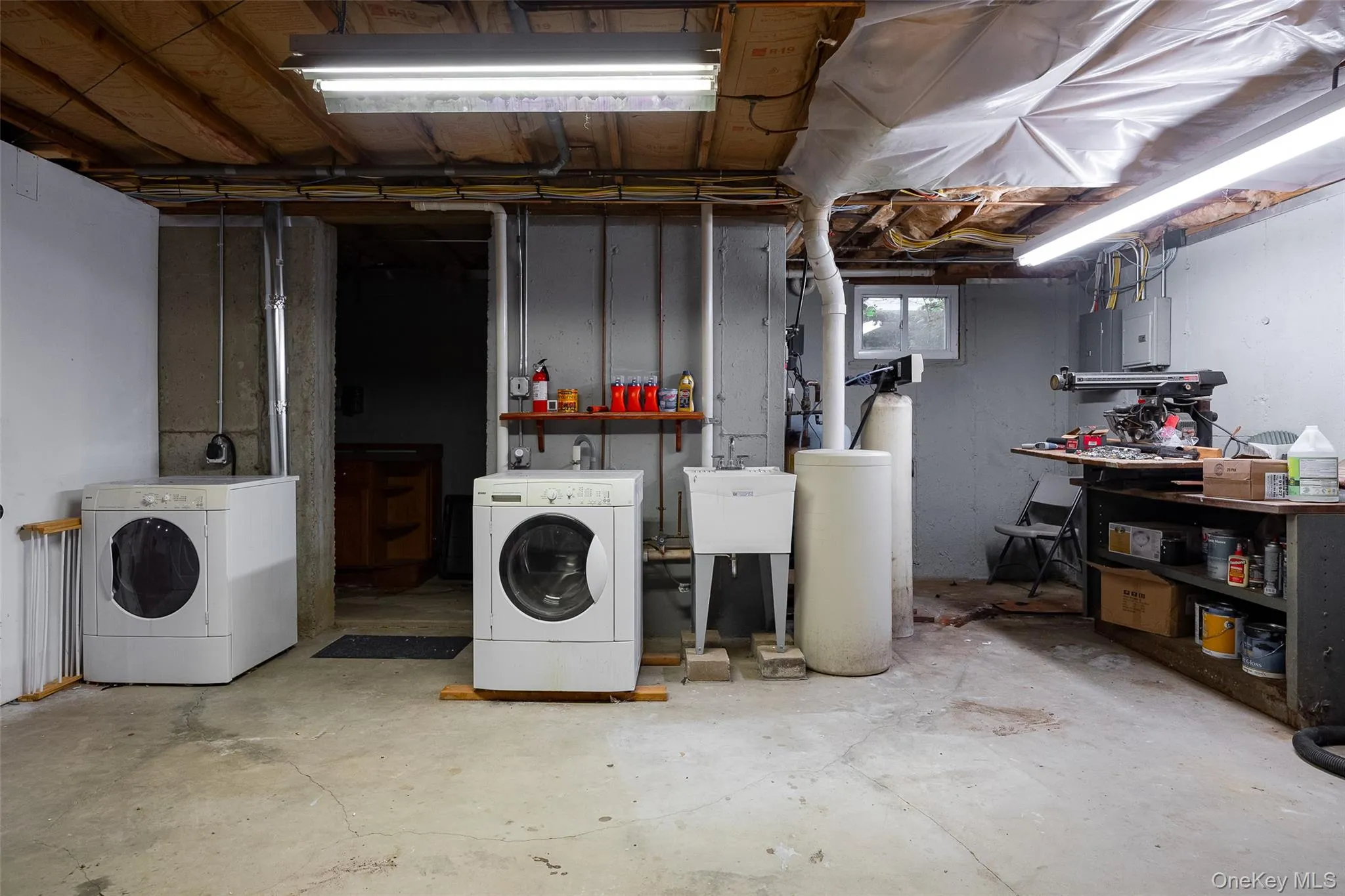 Utility room featuring exposed ceiling joists, concrete flooring, a wall-mounted utility sink, and visible plumbing Utility room featuring exposed ceiling joists, concrete flooring, a wall-mounted utility sink, and visible plumbing