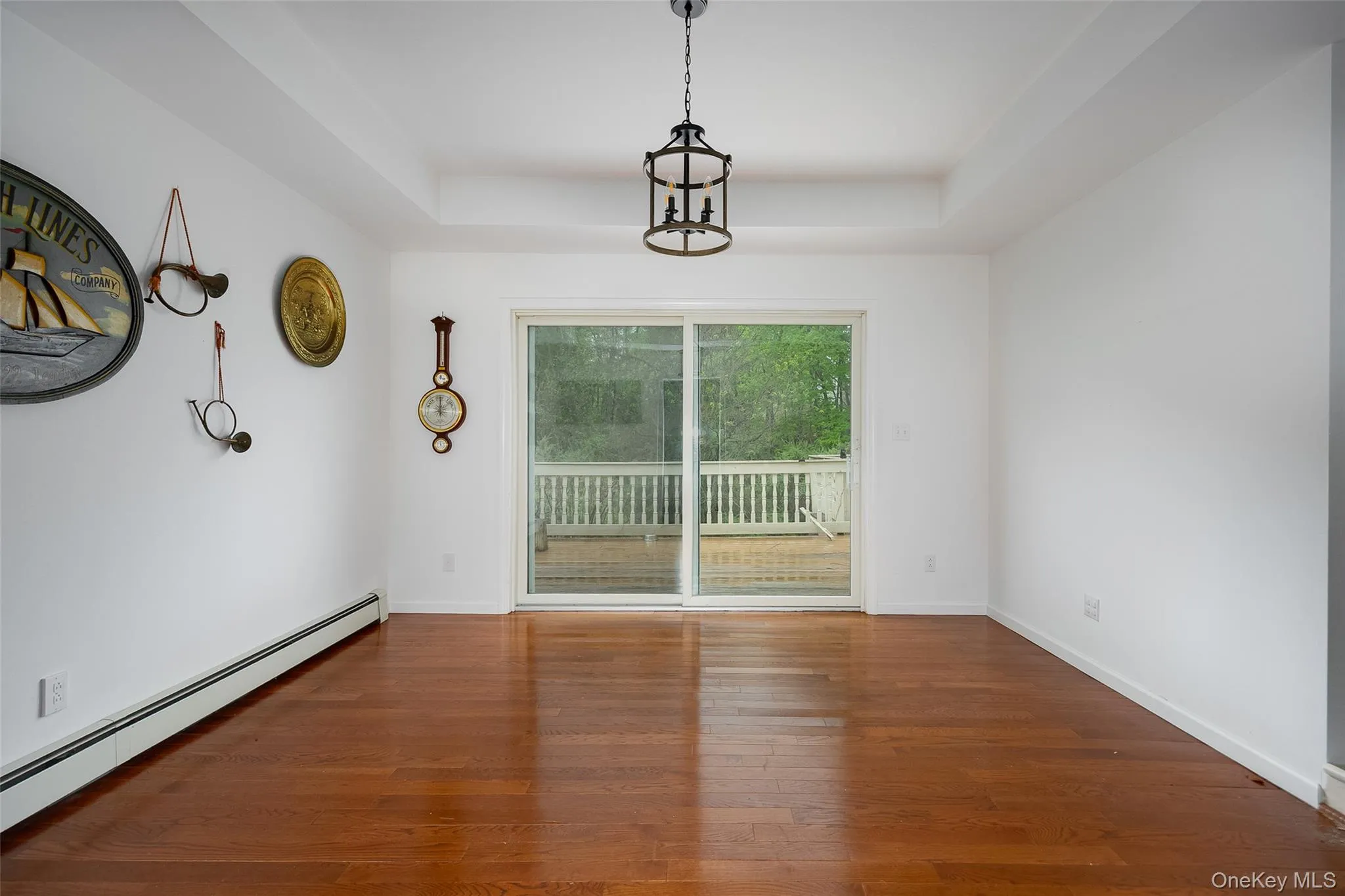 Spacious room featuring wood-finish flooring, a tray ceiling, and a dark metal chandelier Spacious room featuring wood-finish flooring, a tray ceiling, and a dark metal chandelier