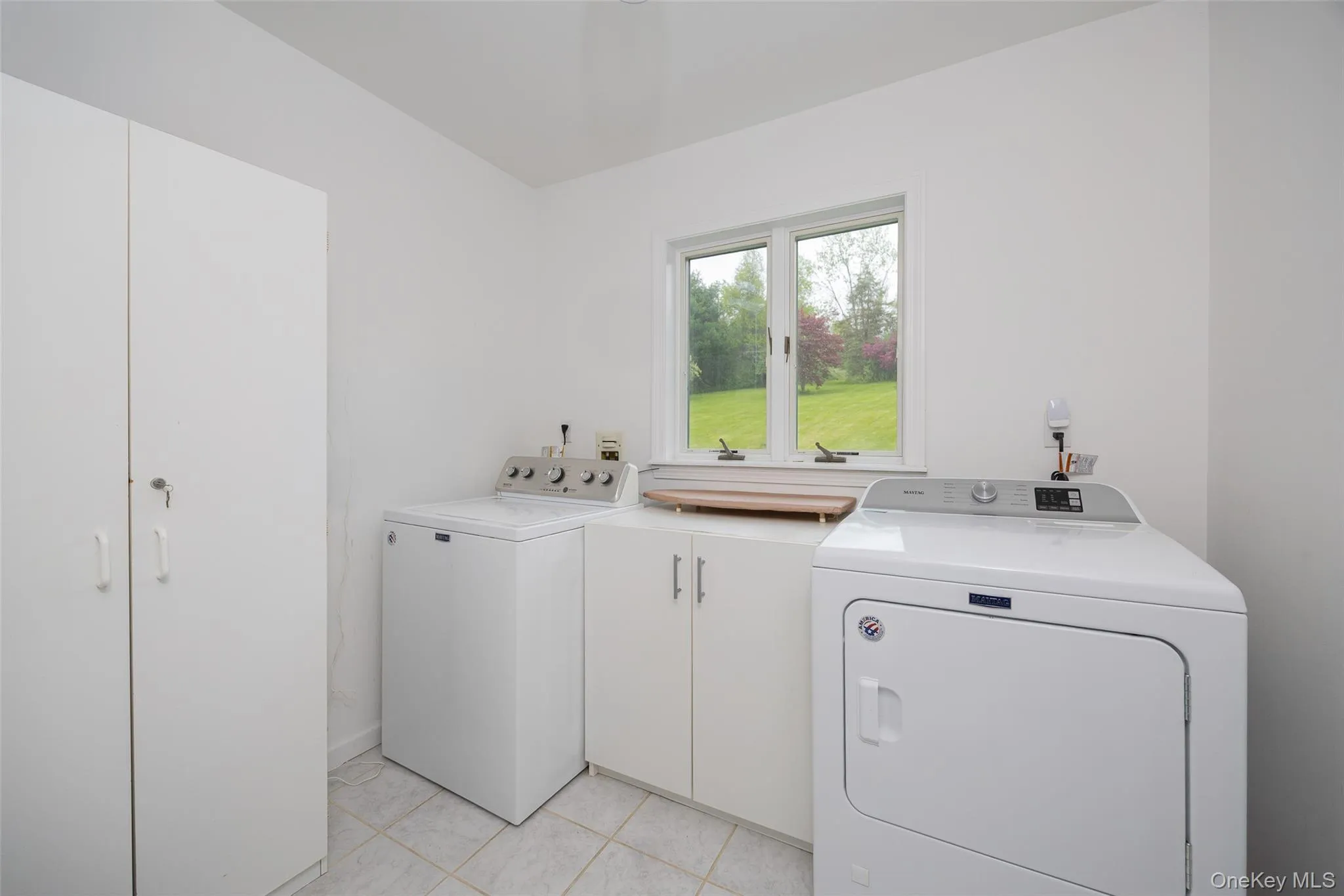 Dedicated laundry space featuring white cabinetry, a large window, tiled flooring, and a built-in countertop Dedicated laundry space featuring white cabinetry, a large window, tiled flooring, and a built-in countertop