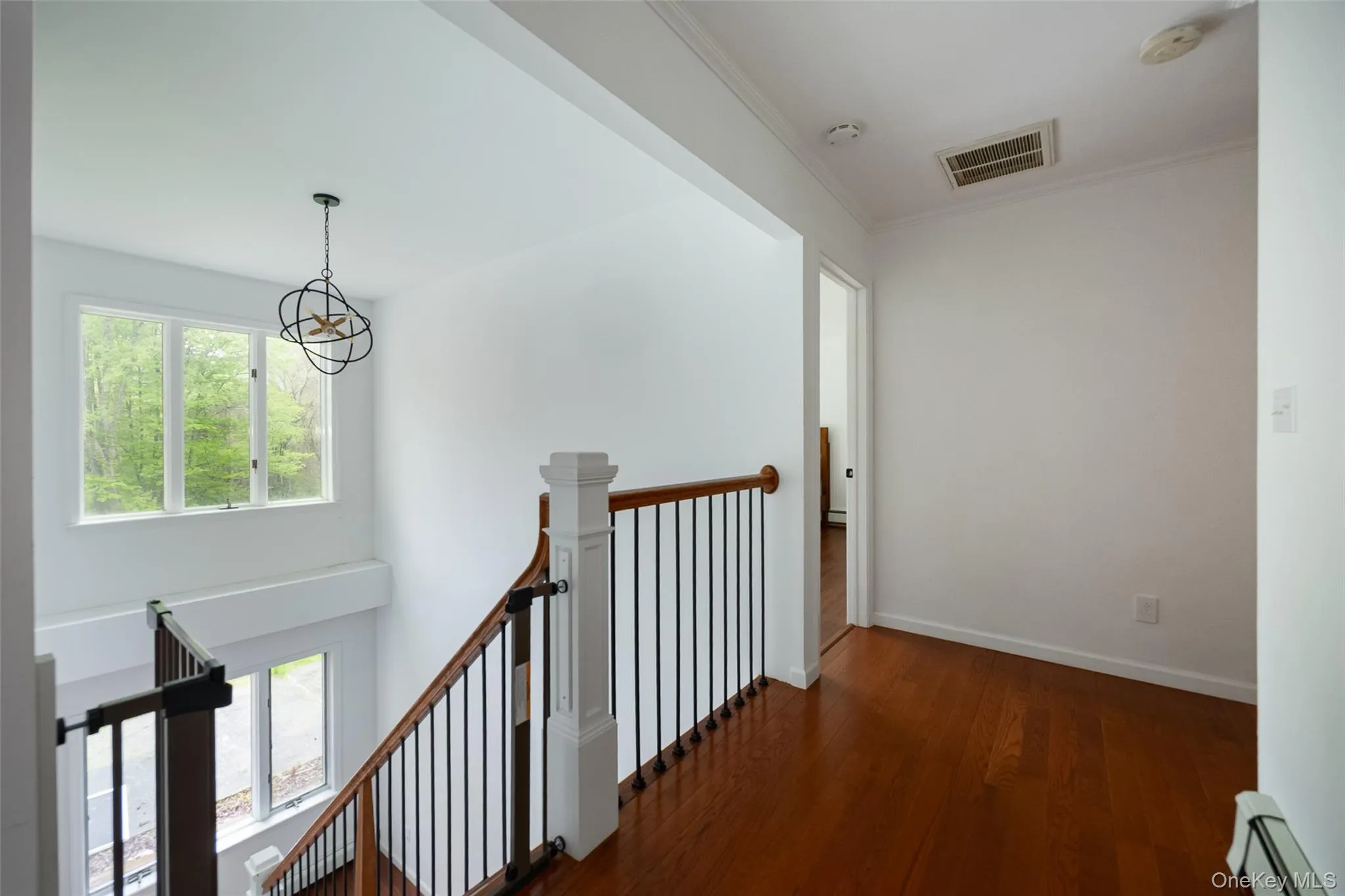 Upper-level landing featuring wood-finish flooring, a contemporary chandelier, a white balustrade with dark spindles, and natural light from multiple windows Upper-level landing featuring wood-finish flooring, a contemporary chandelier, a white balustrade with dark spindles, and natural light from multiple windows
