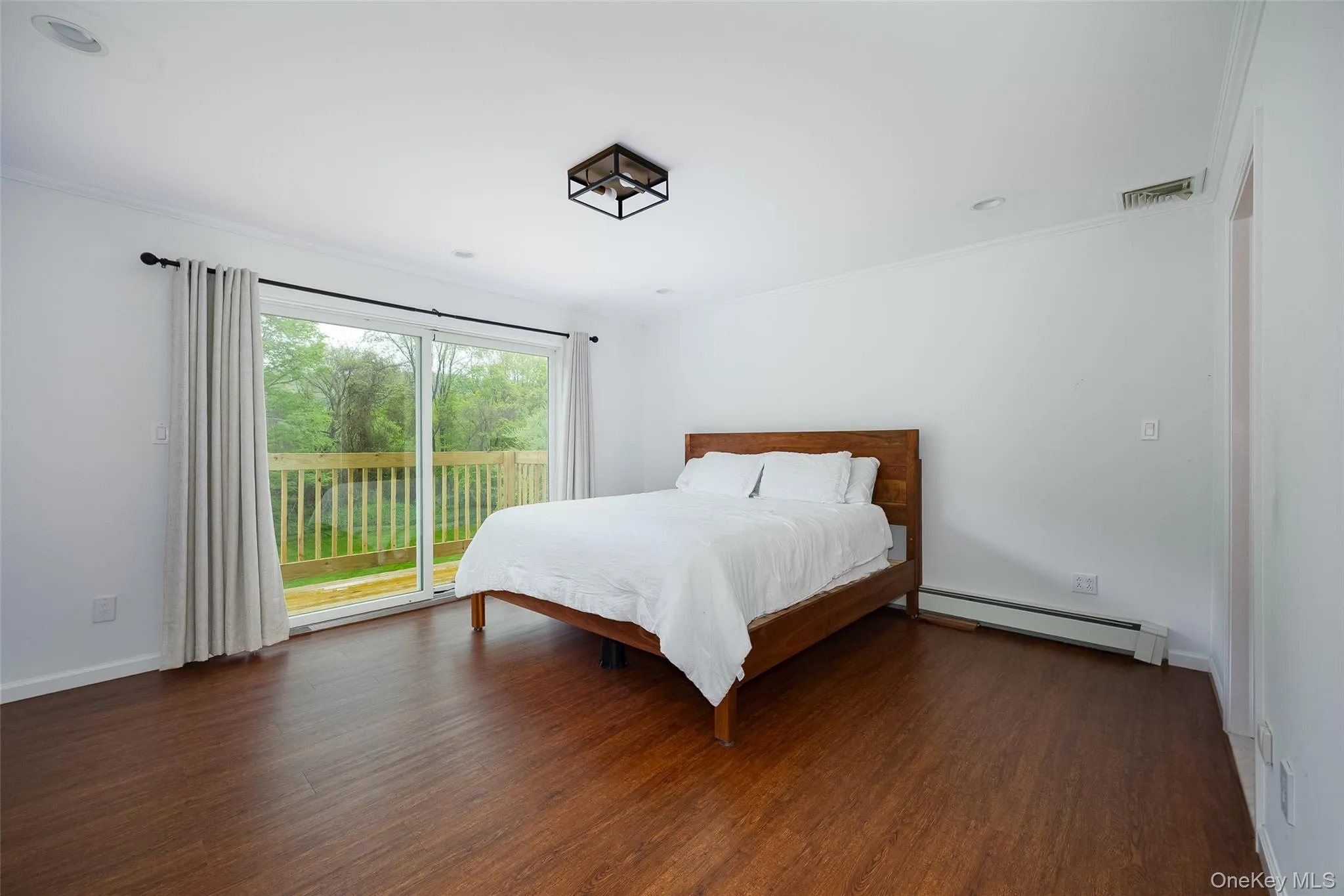 Spacious room with wood-finish flooring, a large sliding glass door opening to an outdoor deck with wood railings, a ceiling-mounted light fixture, and white painted walls Spacious room with wood-finish flooring, a large sliding glass door opening to an outdoor deck with wood railings, a ceiling-mounted light fixture, and white painted walls