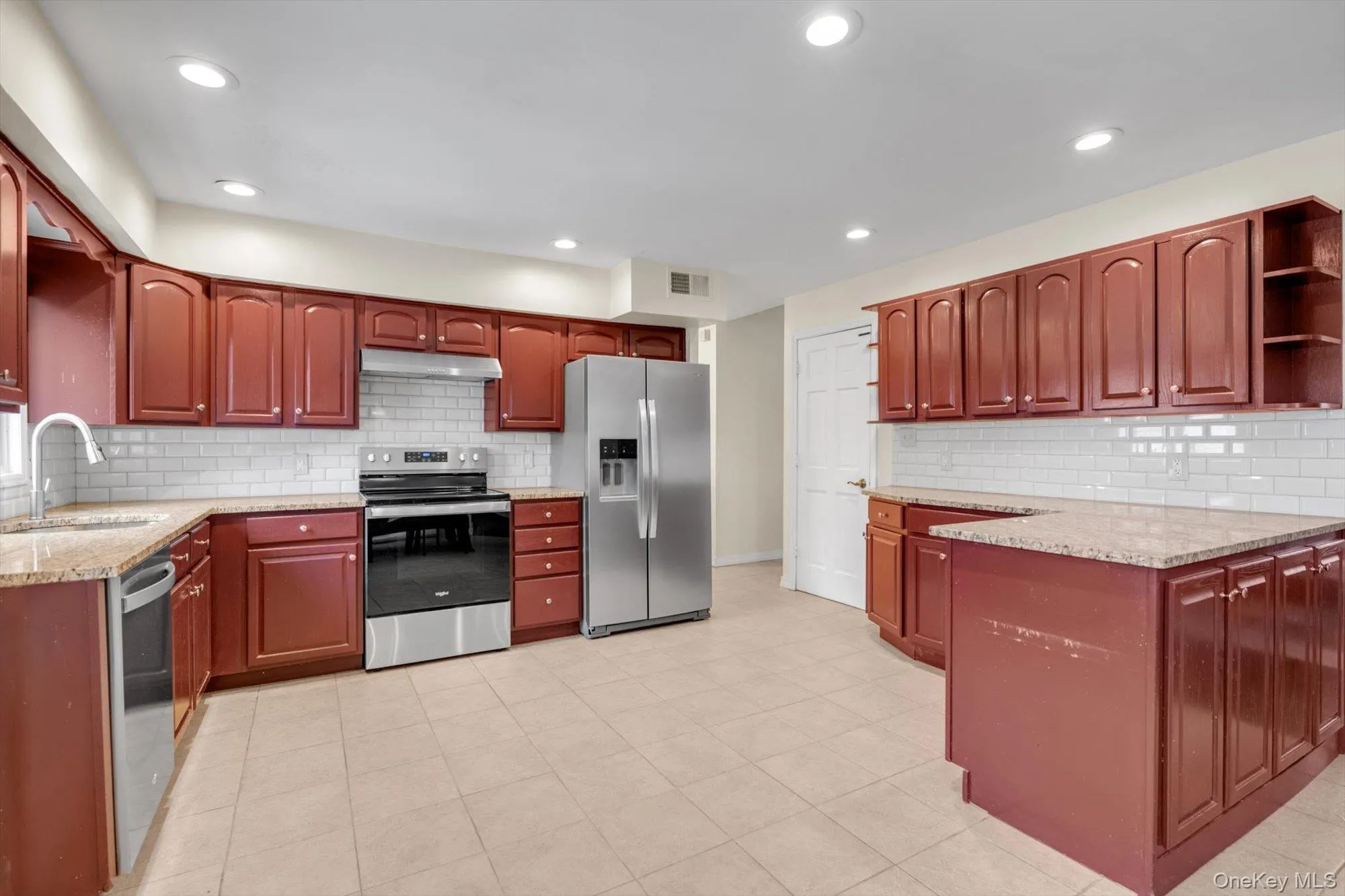 Kitchen featuring wood-finish cabinetry, light-toned countertops, tile flooring, stainless steel appliances, and a subway tile backsplash Kitchen featuring wood-finish cabinetry, light-toned countertops, tile flooring, stainless steel appliances, and a subway tile backsplash