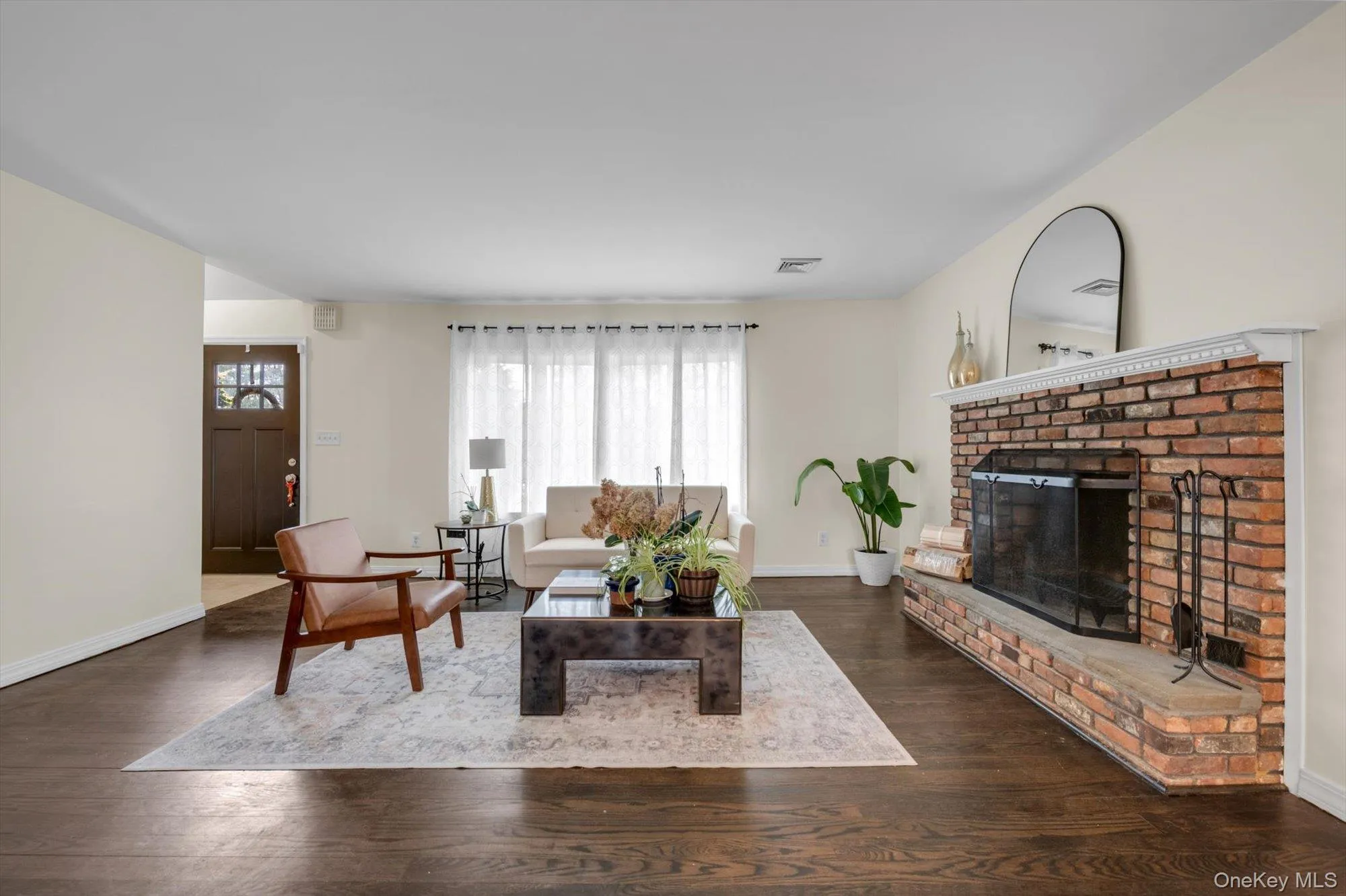 Spacious living area featuring a brick fireplace with a stone hearth, dark wood-finish flooring, and white walls Spacious living area featuring a brick fireplace with a stone hearth, dark wood-finish flooring, and white walls