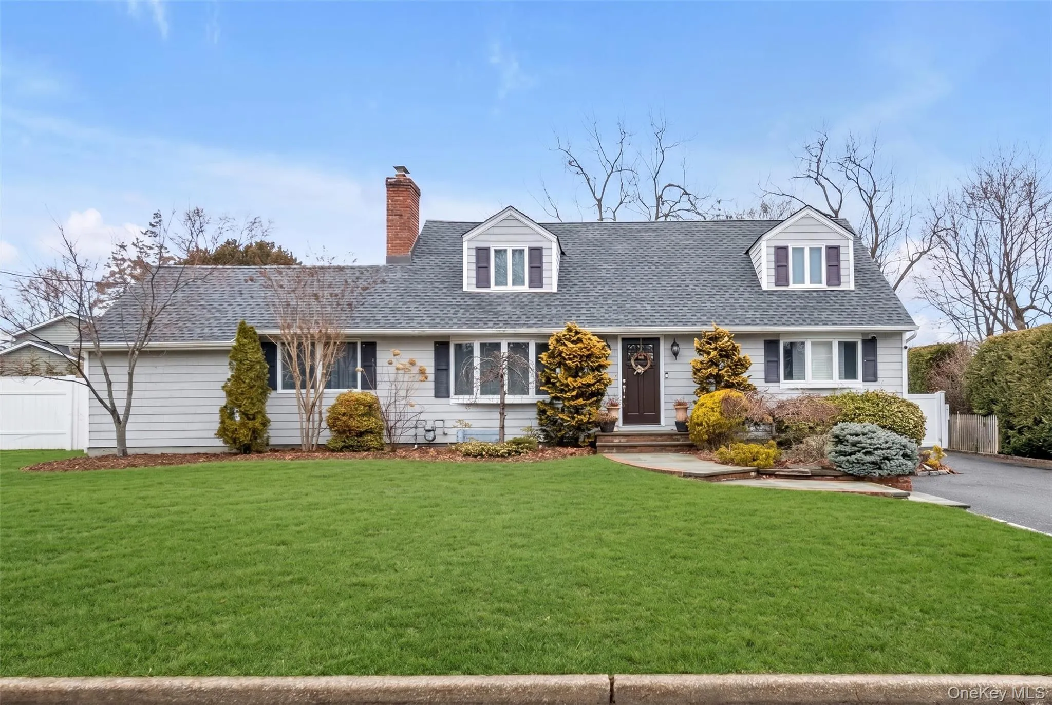 Classic Cape Cod style residence featuring light gray siding and a dark shingle roof Classic Cape Cod style residence featuring light gray siding and a dark shingle roof