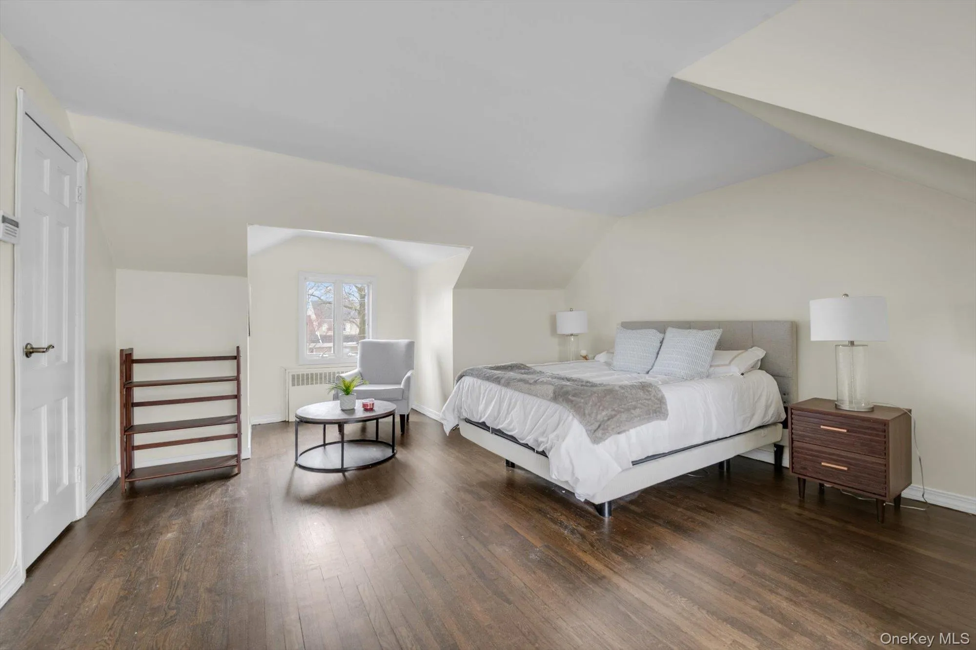 Spacious room with dark wood-finish flooring, light-toned walls, and a window dormer Spacious room with dark wood-finish flooring, light-toned walls, and a window dormer