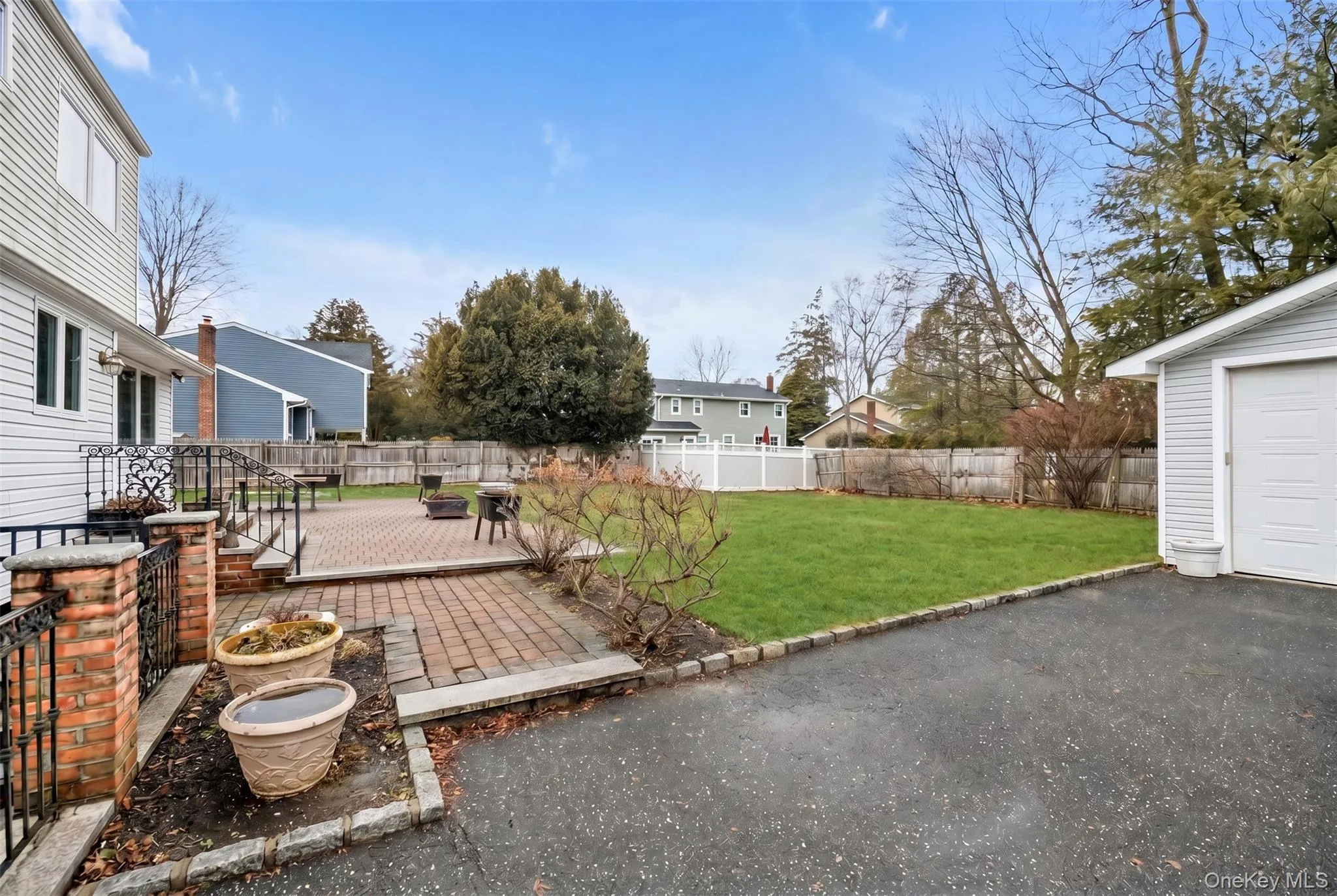 Expansive backyard featuring a brick paver patio, a lush green lawn, mature trees, and a detached garage with a white panel door Expansive backyard featuring a brick paver patio, a lush green lawn, mature trees, and a detached garage with a white panel door