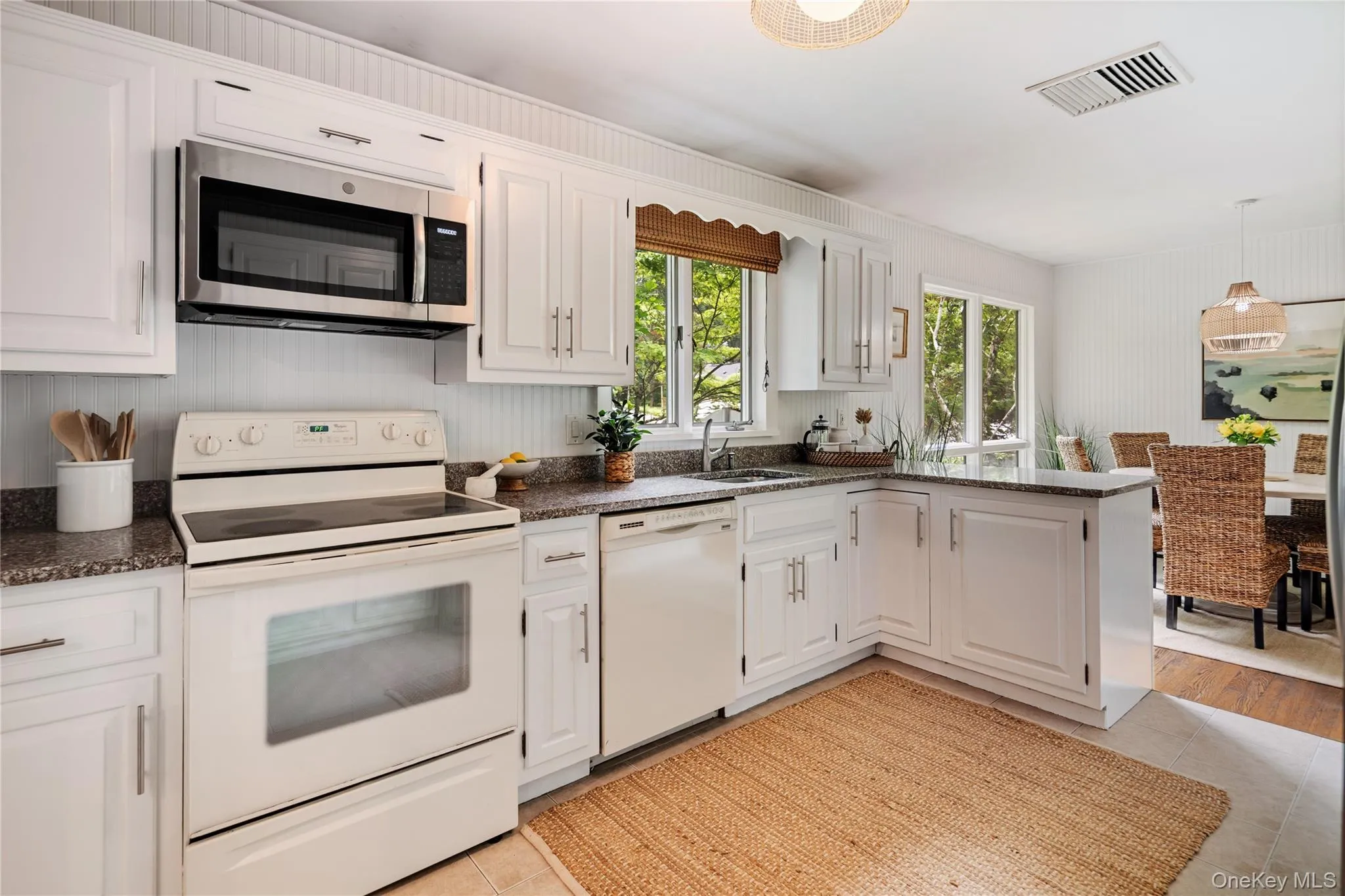 The kitchen boasts plenty of cabinets and counter space, with an oversink window that lets in sunlight and offers lovely garden views. Beadboard walls add to its charming appeal. The kitchen boasts plenty of cabinets and counter space, with an oversink window that lets in sunlight and offers lovely garden views. Beadboard walls add to its charming appeal.