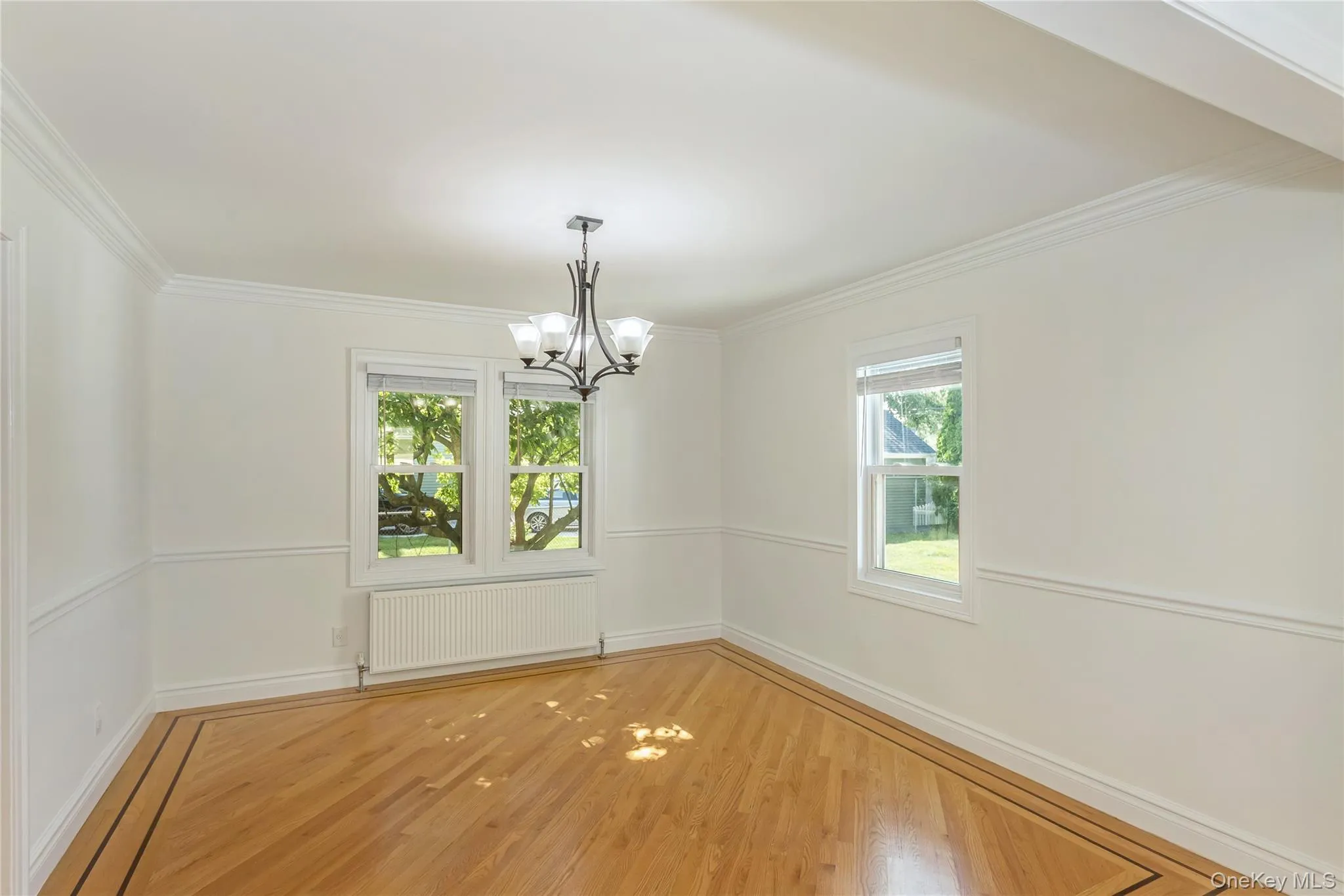 Unfurnished dining area with wood finished floors, radiator, crown molding, and a chandelier Unfurnished dining area with wood finished floors, radiator, crown molding, and a chandelier