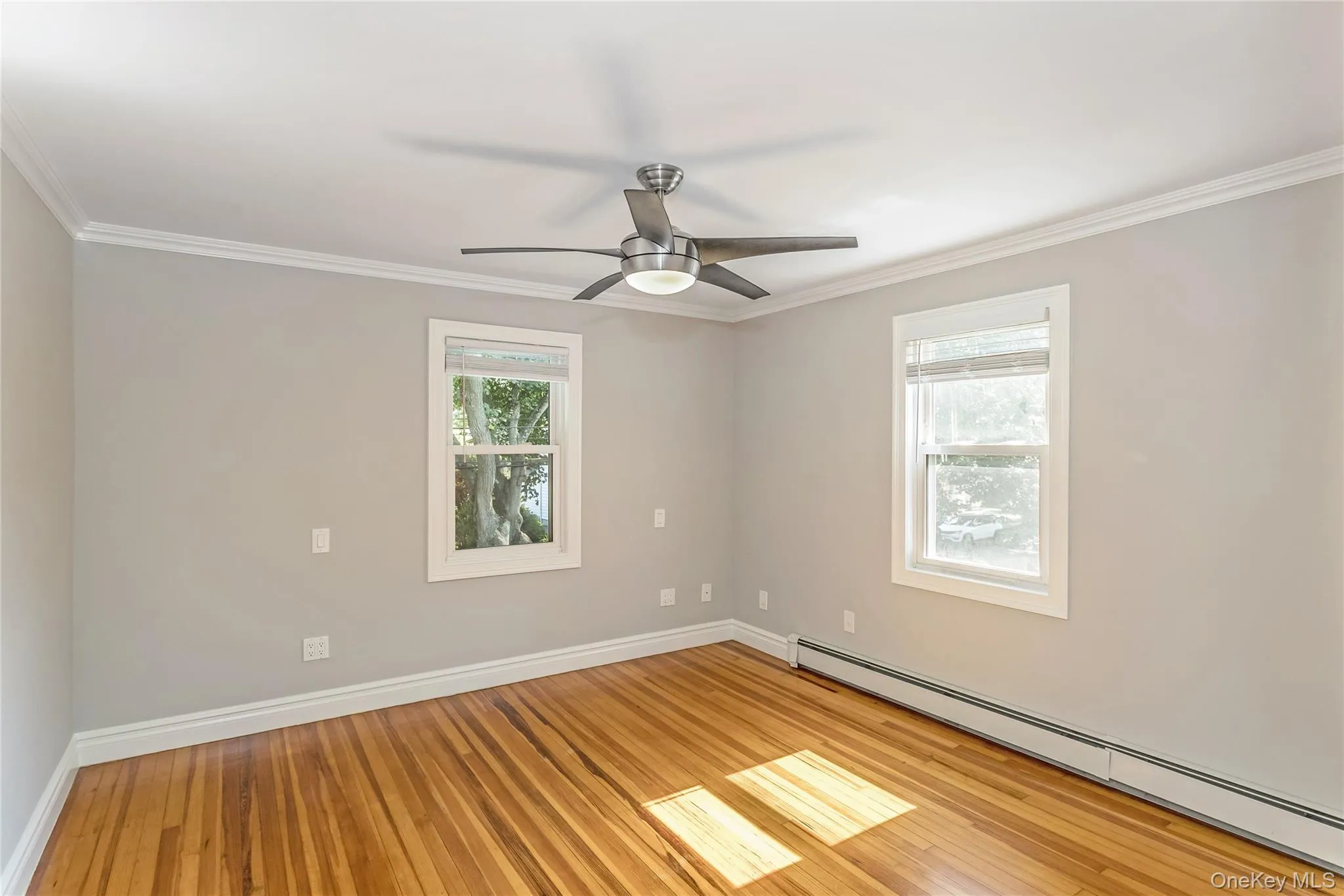Spare room with baseboard heating, ornamental molding, light wood-style flooring, and ceiling fan Spare room with baseboard heating, ornamental molding, light wood-style flooring, and ceiling fan