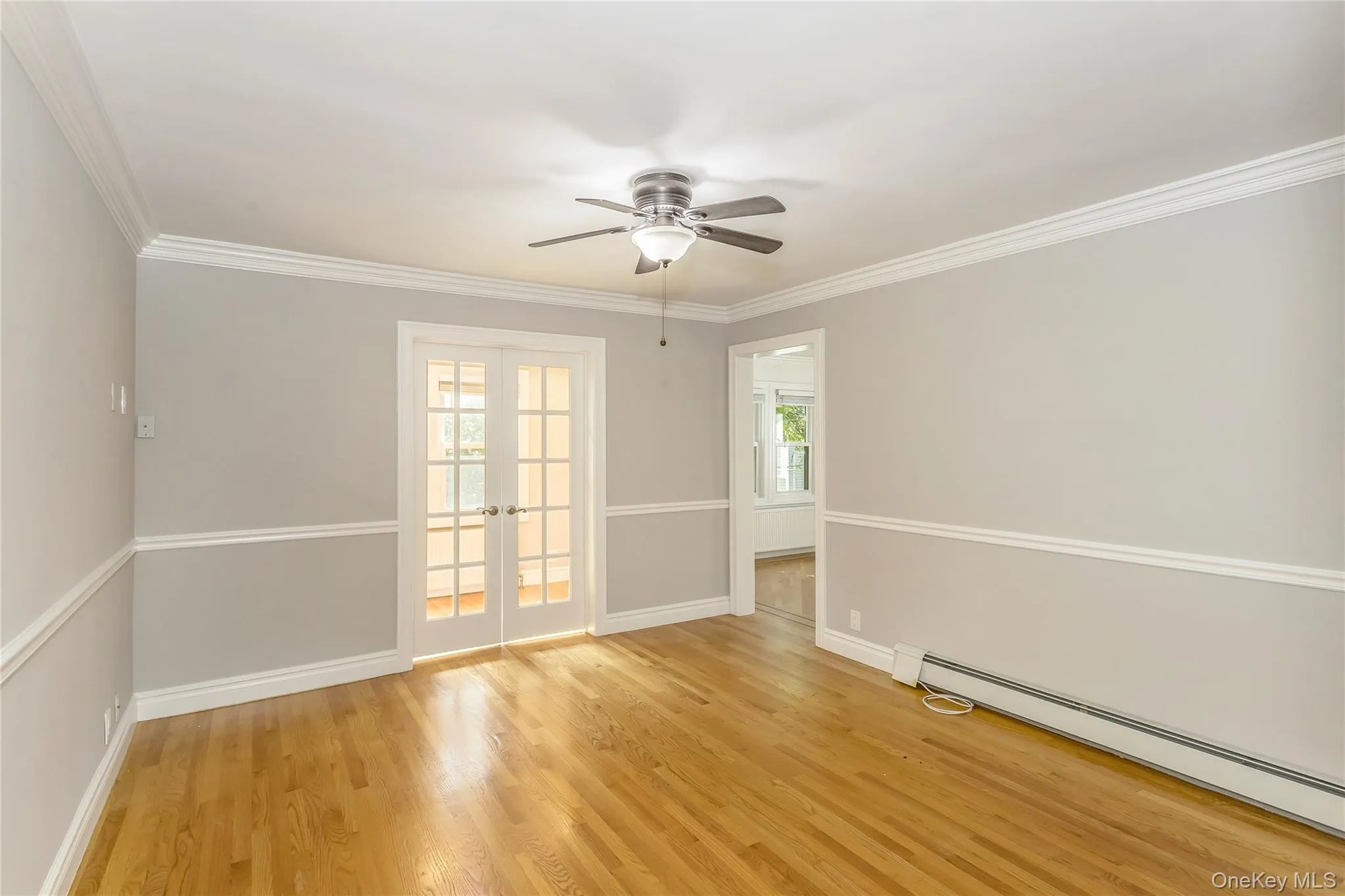 Spare room with ornamental molding, light wood-type flooring, a baseboard heating unit, french doors, and ceiling fan Spare room with ornamental molding, light wood-type flooring, a baseboard heating unit, french doors, and ceiling fan