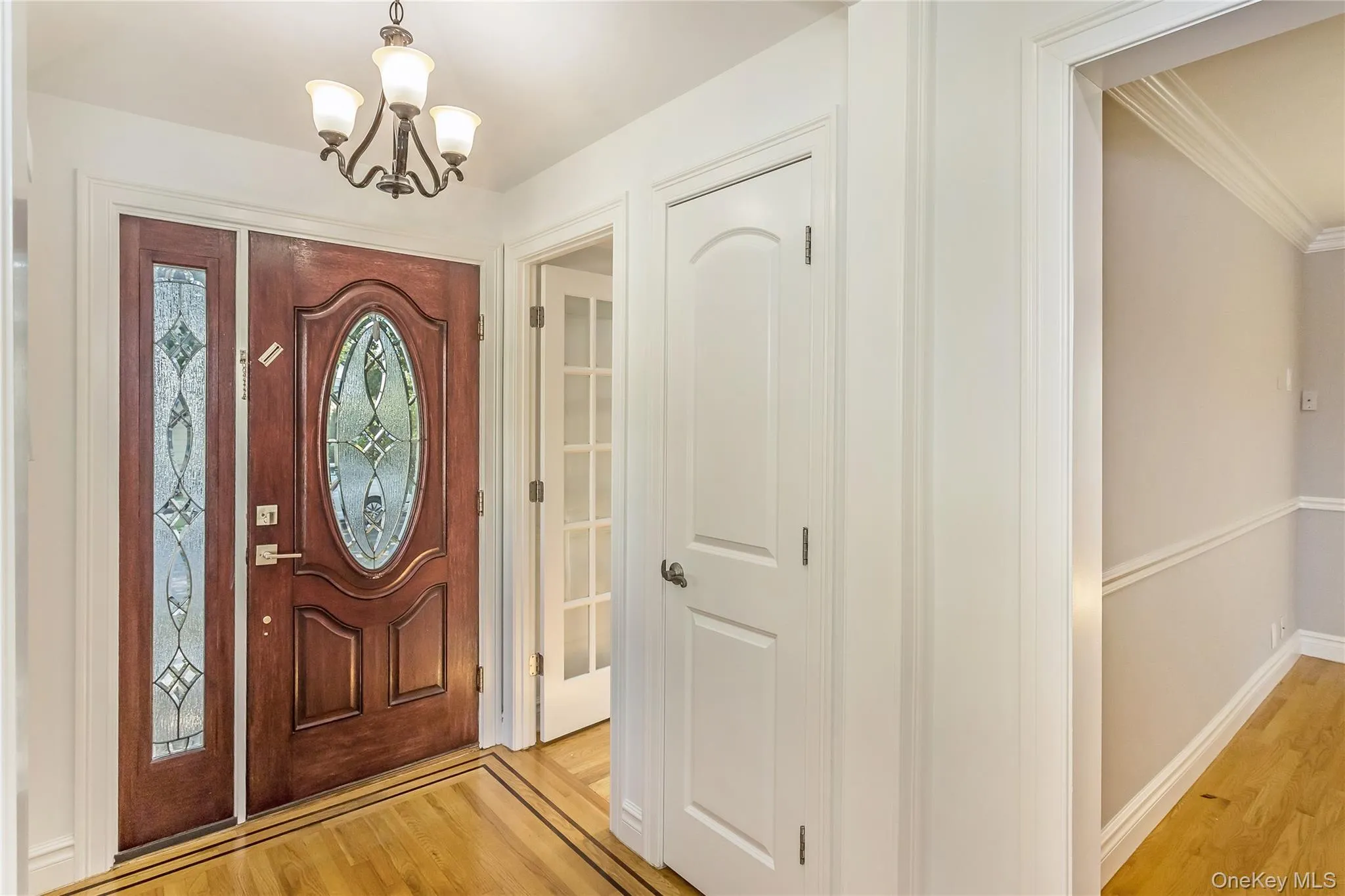 Foyer entrance with light wood-type flooring, a chandelier, and ornamental molding Foyer entrance with light wood-type flooring, a chandelier, and ornamental molding