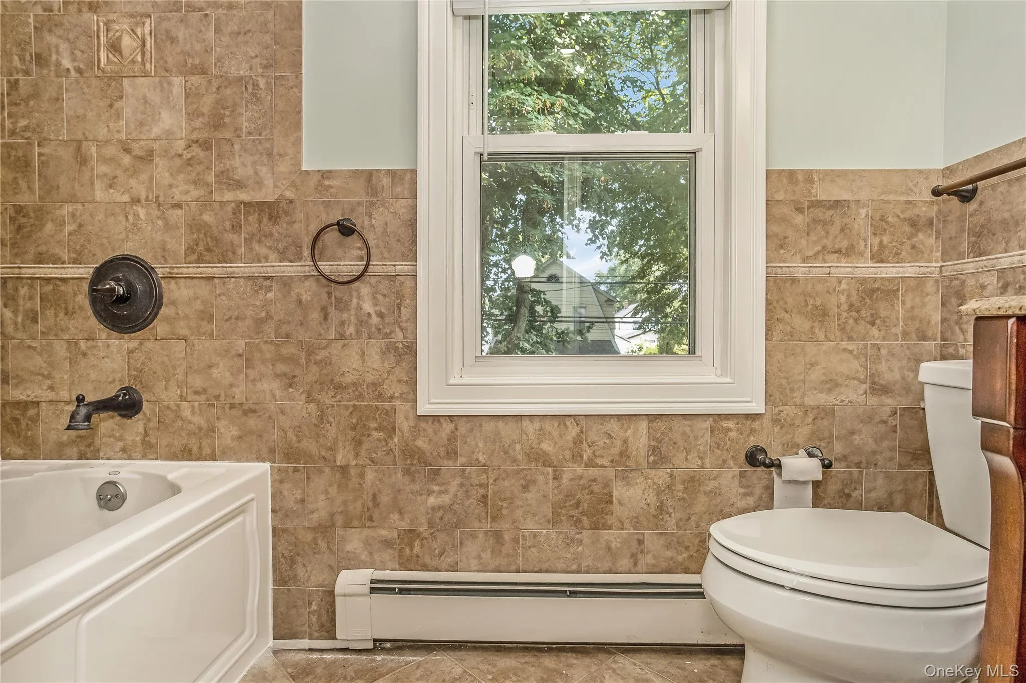 Full bathroom featuring tile walls, a baseboard heating unit, tile patterned flooring, and bathing tub / shower combination Full bathroom featuring tile walls, a baseboard heating unit, tile patterned flooring, and bathing tub / shower combination