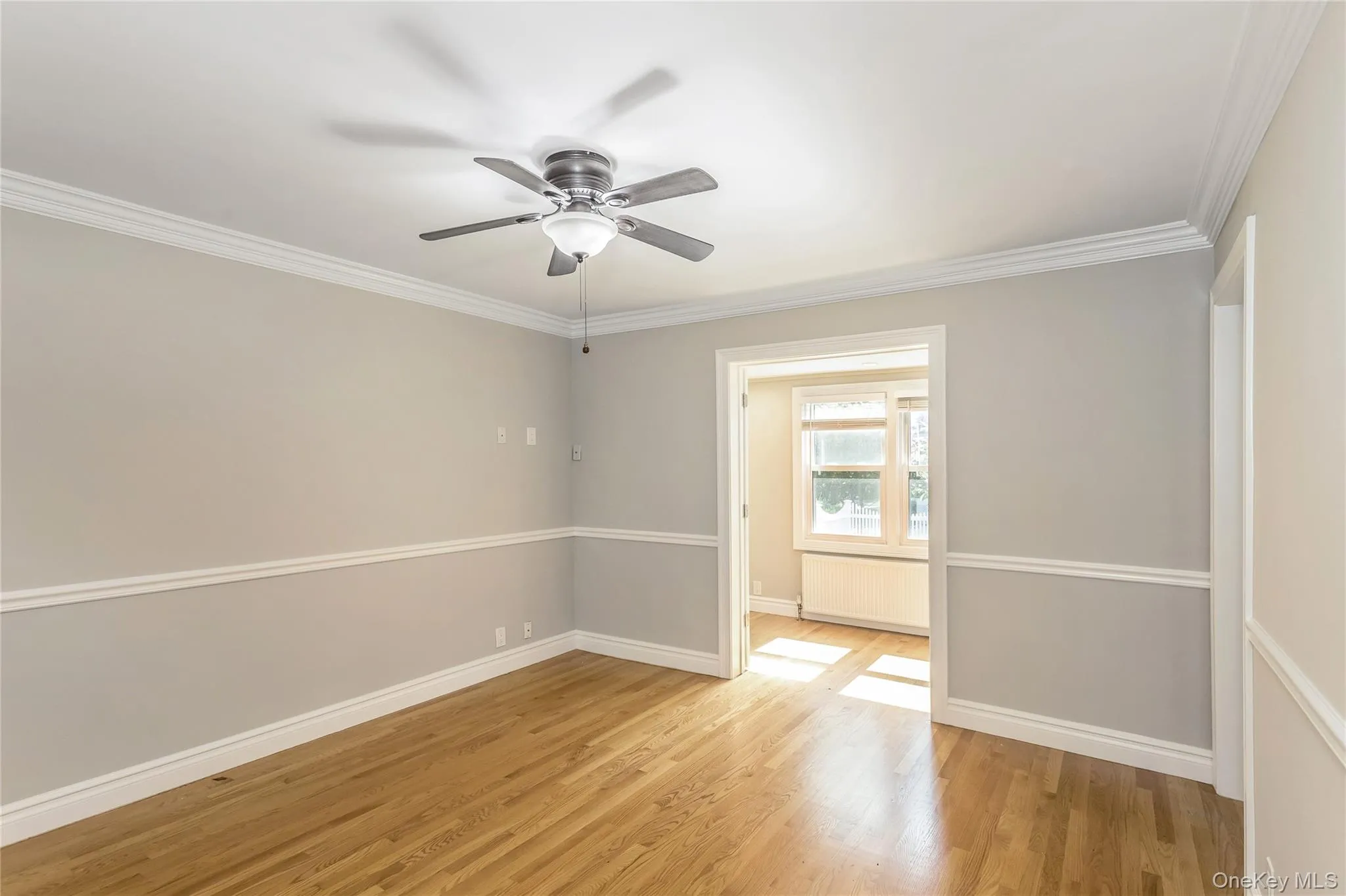 Empty room with ornamental molding, light wood-type flooring, ceiling fan, and radiator heating unit Empty room with ornamental molding, light wood-type flooring, ceiling fan, and radiator heating unit