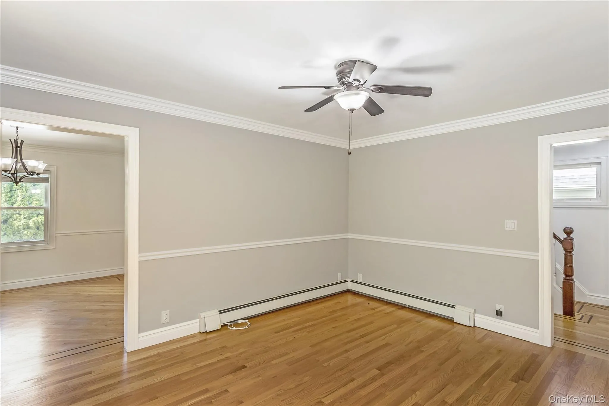 Unfurnished room featuring ornamental molding, light wood-type flooring, a chandelier, baseboard heating, and ceiling fan Unfurnished room featuring ornamental molding, light wood-type flooring, a chandelier, baseboard heating, and ceiling fan