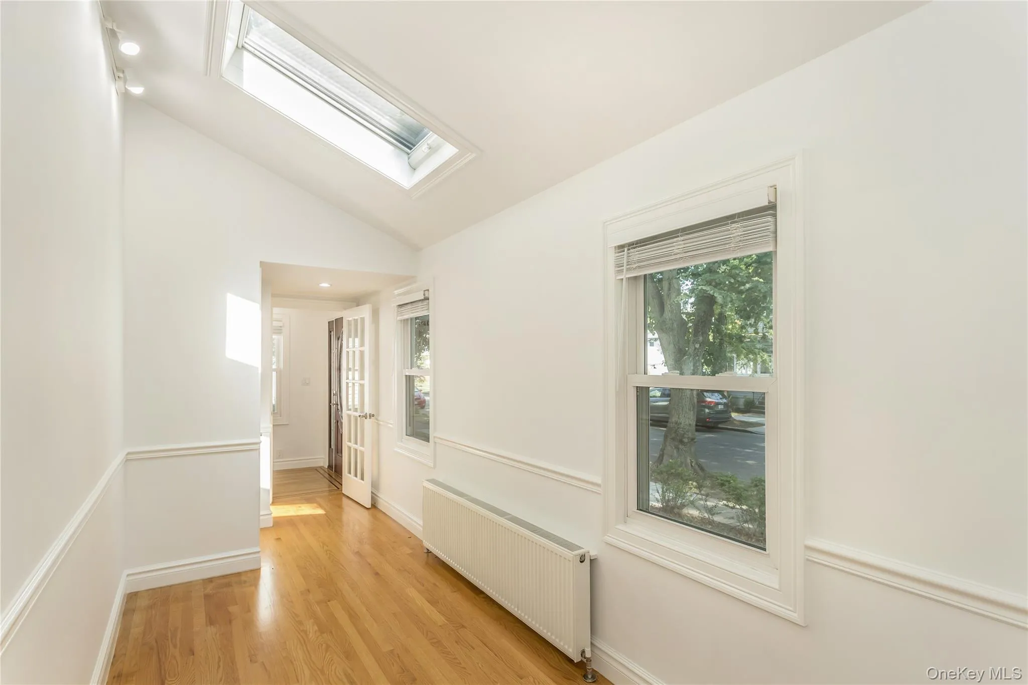 Hall featuring plenty of natural light, radiator, lofted ceiling, light wood finished floors, and a skylight Hall featuring plenty of natural light, radiator, lofted ceiling, light wood finished floors, and a skylight