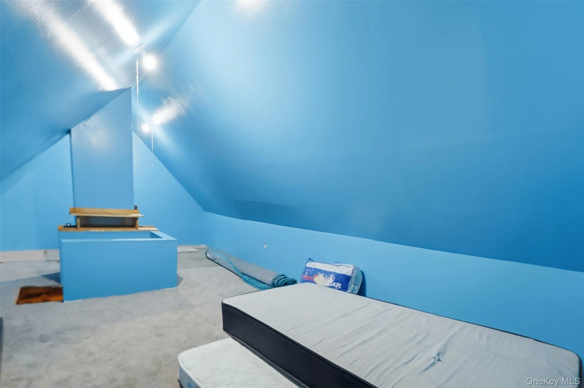 Attic space featuring sloped ceilings, light blue wall paint, gray carpeting, and a central architectural column with a wooden top detail Attic space featuring sloped ceilings, light blue wall paint, gray carpeting, and a central architectural column with a wooden top detail