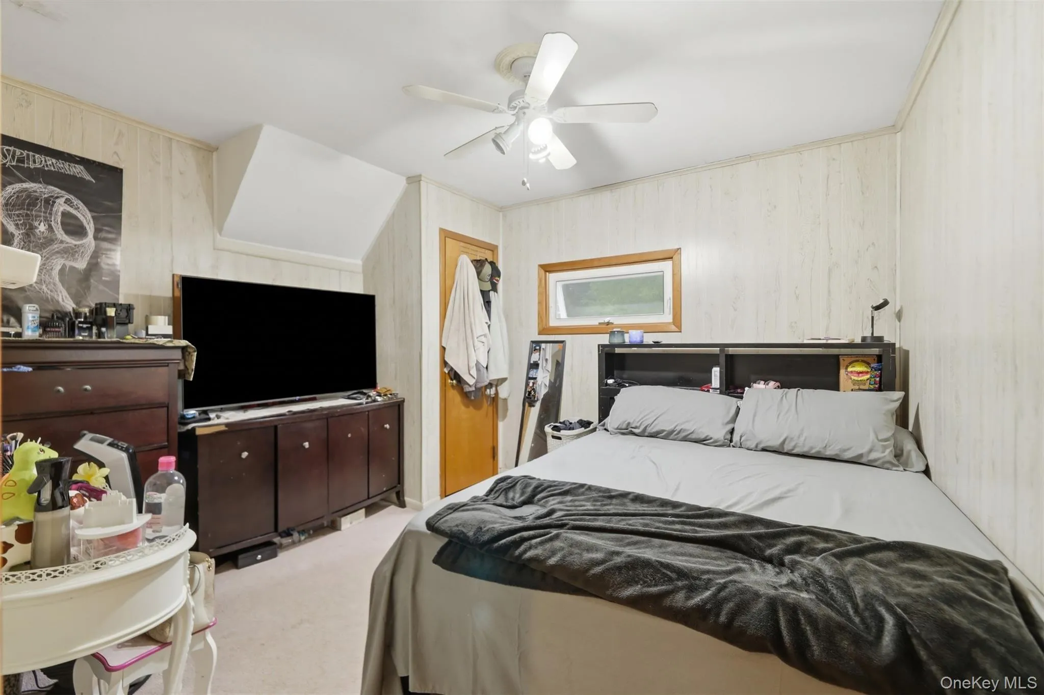 Bedroom featuring light-toned vertical wall paneling, a ceiling fan with integrated lighting, and carpet flooring Bedroom featuring light-toned vertical wall paneling, a ceiling fan with integrated lighting, and carpet flooring