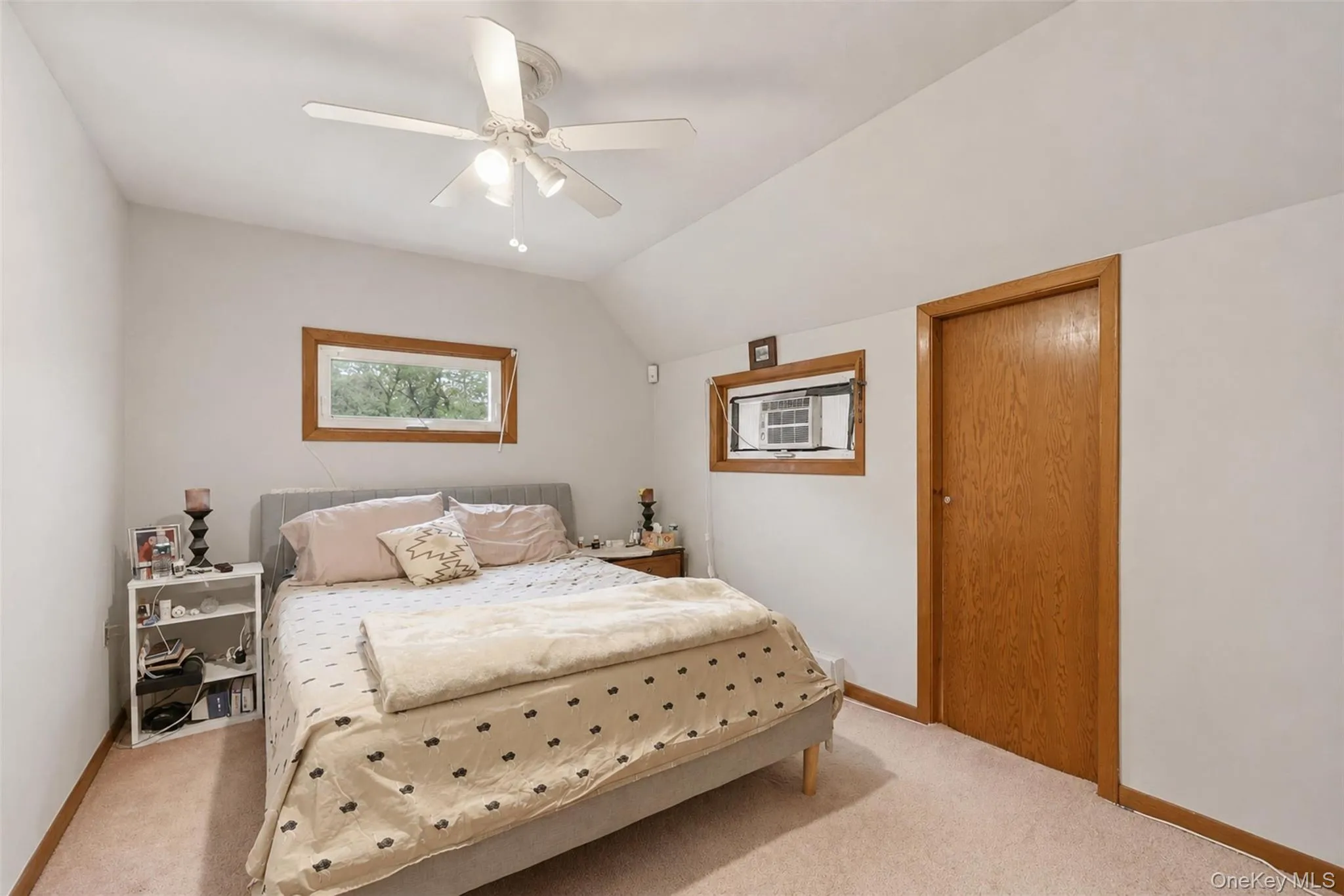 Bedroom featuring sloped ceilings, a ceiling fan with integrated lighting, wood-trimmed windows, a wood-finish door, and carpeting Bedroom featuring sloped ceilings, a ceiling fan with integrated lighting, wood-trimmed windows, a wood-finish door, and carpeting