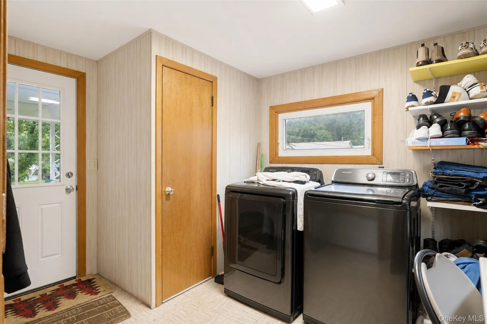 Utility room featuring a window with wood trim, a built-in shelving unit, and a white paneled door with glass inserts Utility room featuring a window with wood trim, a built-in shelving unit, and a white paneled door with glass inserts