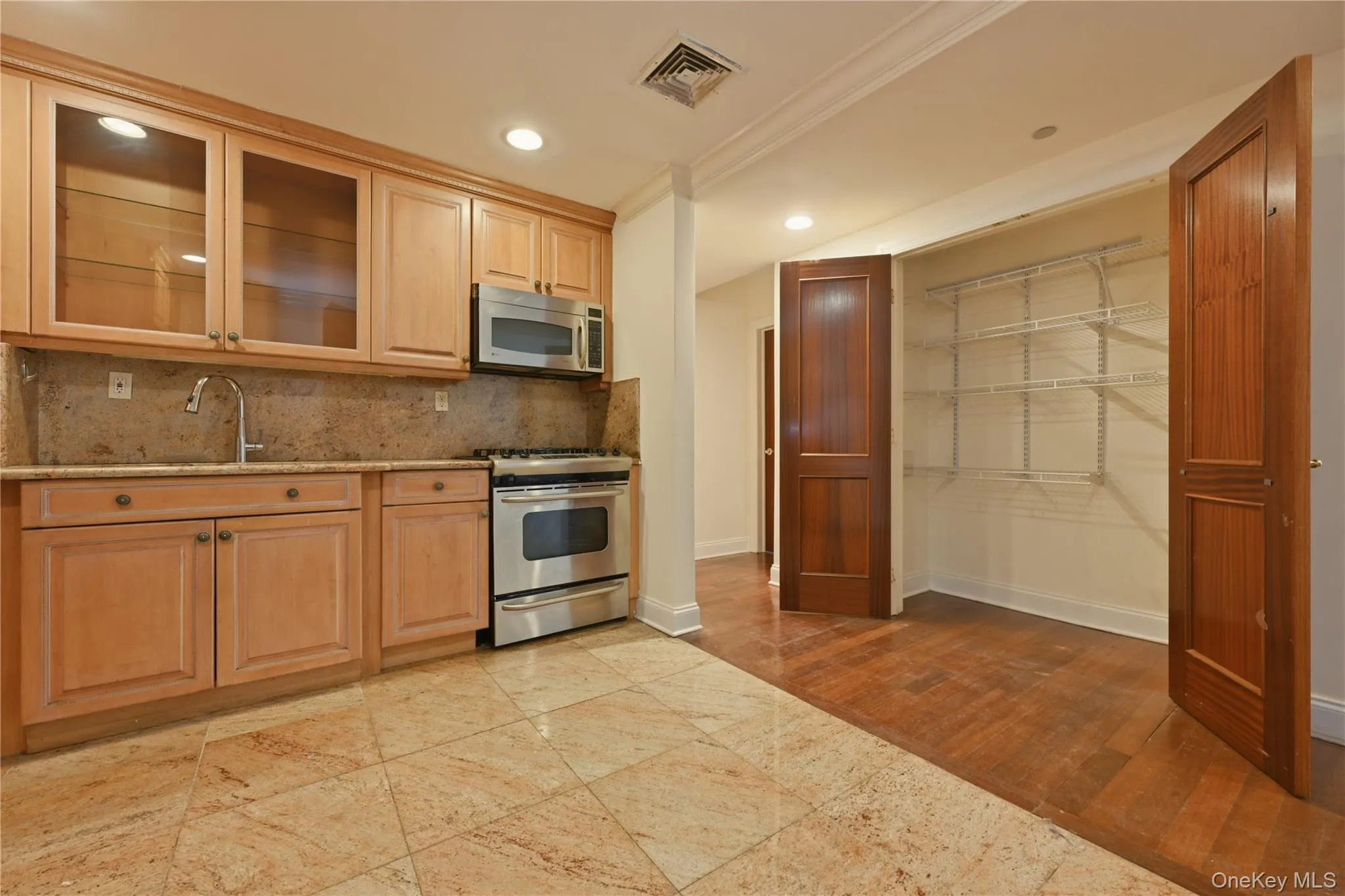 Kitchen featuring light wood-finish cabinetry with glass-front uppers, stainless steel appliances, and a stone slab backsplash Kitchen featuring light wood-finish cabinetry with glass-front uppers, stainless steel appliances, and a stone slab backsplash