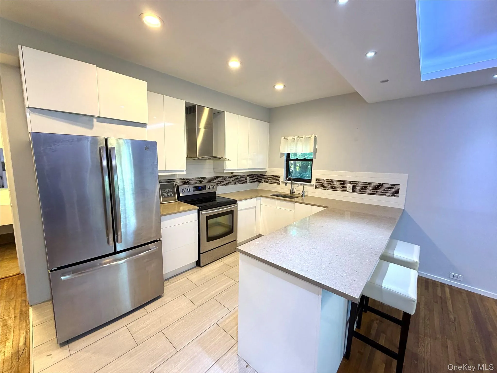 Modern kitchen featuring stainless steel appliances, white cabinetry, a light-colored countertop, and a tiled backsplash Modern kitchen featuring stainless steel appliances, white cabinetry, a light-colored countertop, and a tiled backsplash