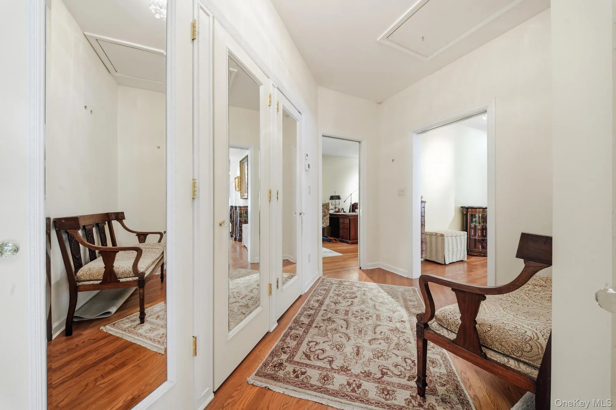 Hallway featuring polished wood flooring, mirrored closet doors, and white painted walls Hallway featuring polished wood flooring, mirrored closet doors, and white painted walls