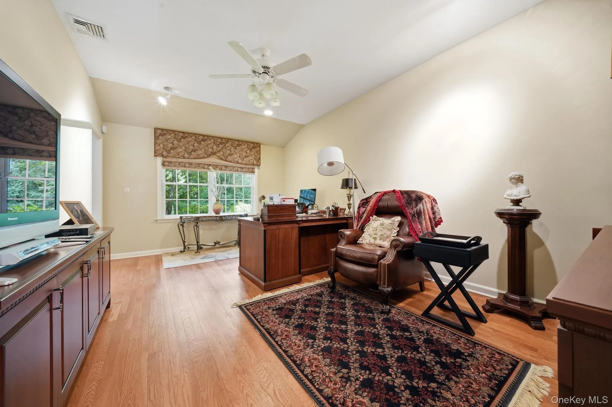 Vaulted ceiling room featuring light wood-finish flooring, a large multi-pane window, and a built-in media console with cabinet storage Vaulted ceiling room featuring light wood-finish flooring, a large multi-pane window, and a built-in media console with cabinet storage