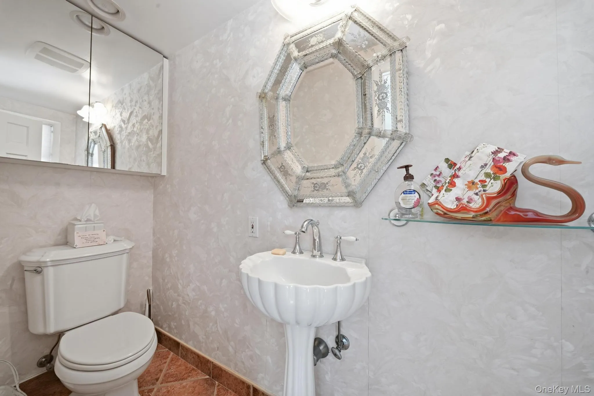 Pedestal sink with fluted basin and chrome fixtures complemented by an ornate octagonal mirror Pedestal sink with fluted basin and chrome fixtures complemented by an ornate octagonal mirror