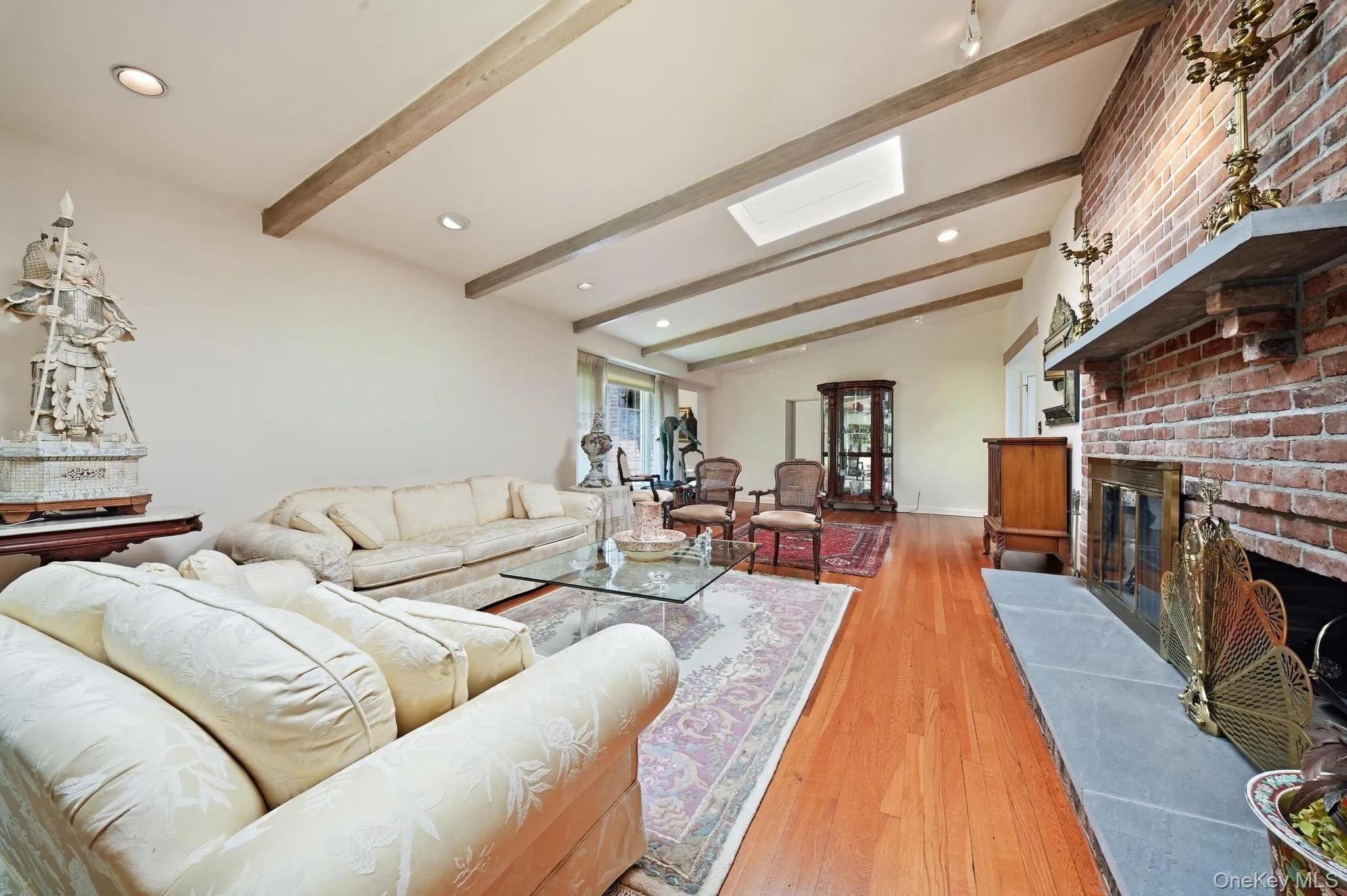Vaulted ceiling with exposed wood beams, brick fireplace with stone hearth, wood-finish flooring, recessed lighting, and a skylight Vaulted ceiling with exposed wood beams, brick fireplace with stone hearth, wood-finish flooring, recessed lighting, and a skylight