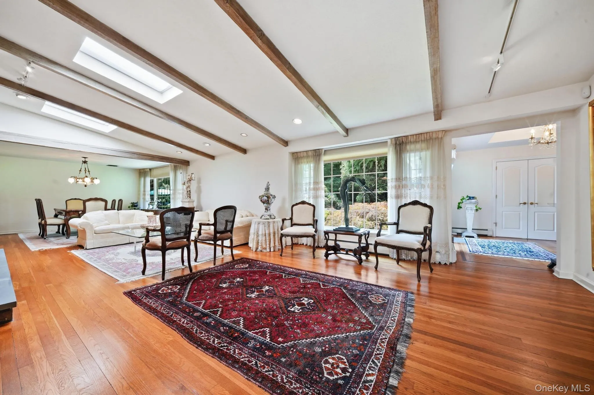Spacious living area featuring wood-finish flooring, exposed ceiling beams, and dual skylights Spacious living area featuring wood-finish flooring, exposed ceiling beams, and dual skylights