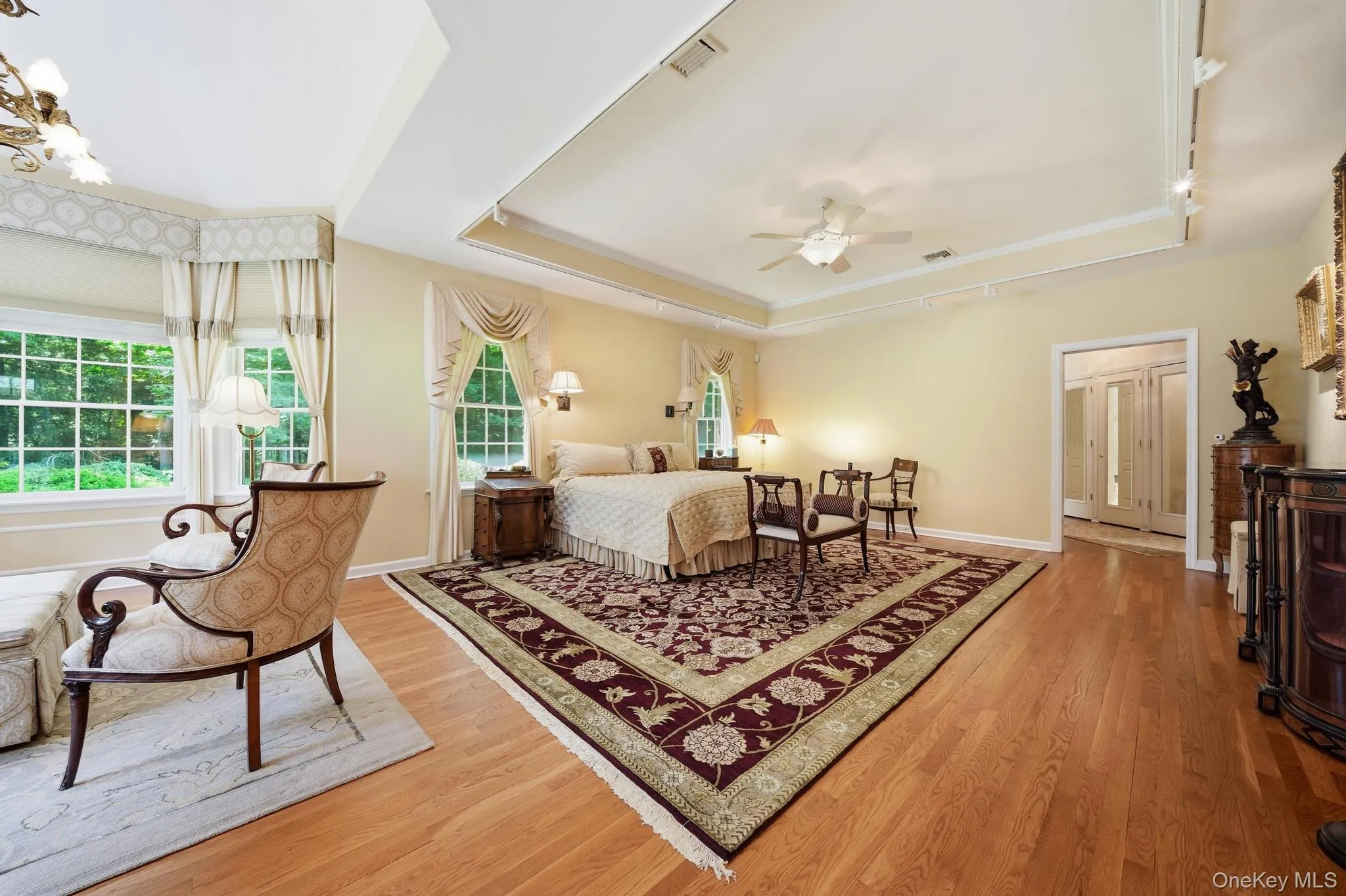 Expansive room featuring light wood-finish flooring, a tray ceiling with a ceiling fan, and multiple windows with decorative valances Expansive room featuring light wood-finish flooring, a tray ceiling with a ceiling fan, and multiple windows with decorative valances