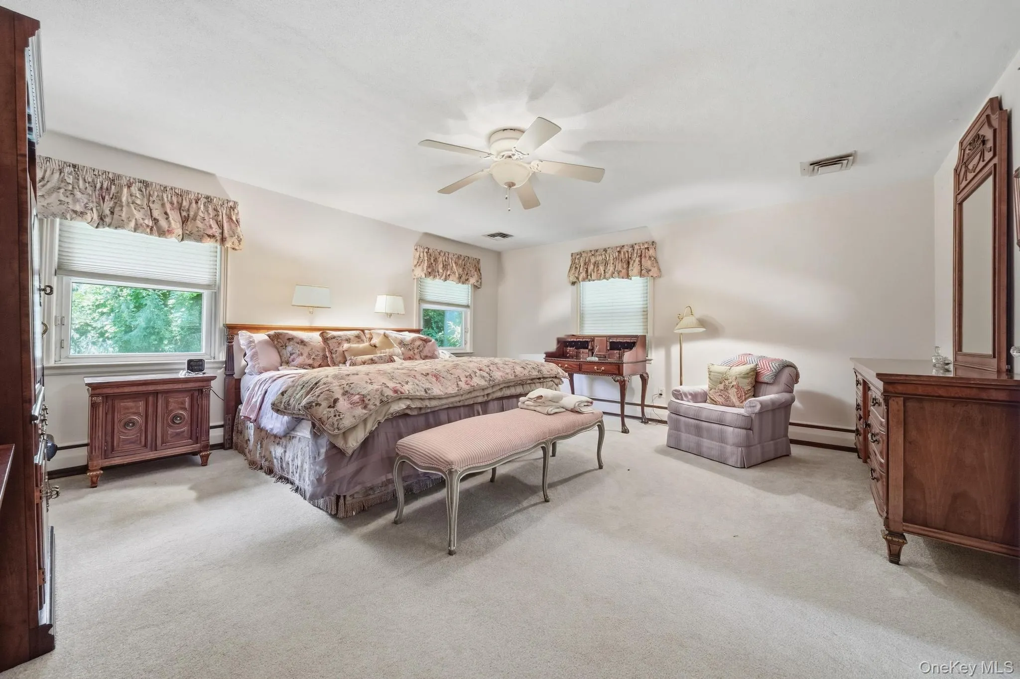 Spacious carpeted room featuring white walls, a ceiling fan, and multiple windows Spacious carpeted room featuring white walls, a ceiling fan, and multiple windows