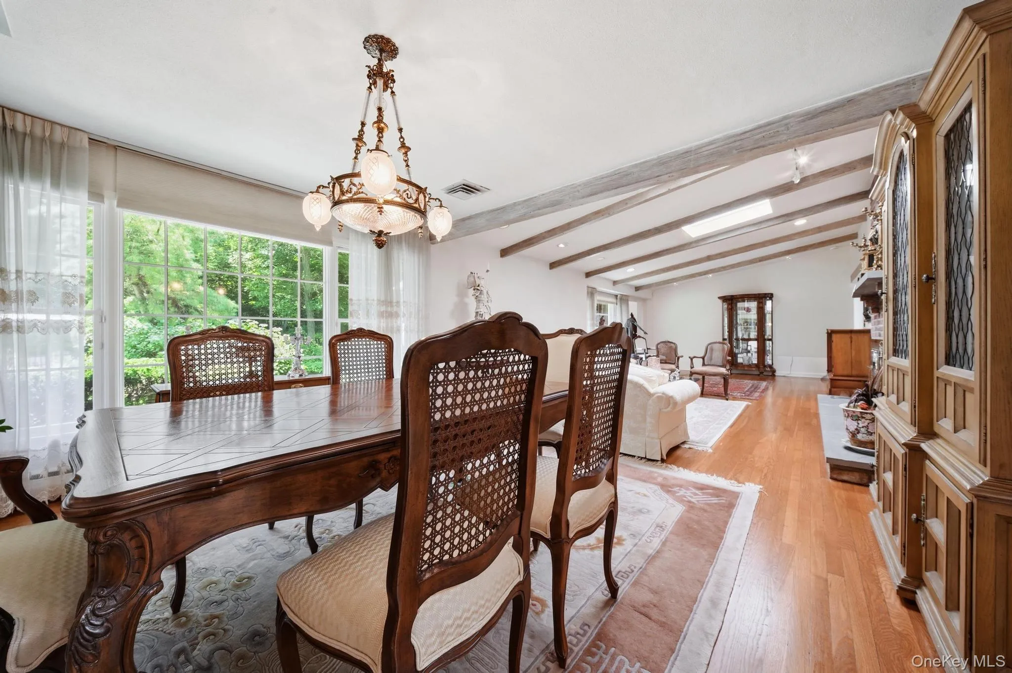 Formal dining area featuring a large window with exterior landscaping, a decorative chandelier, and wood-finish flooring Formal dining area featuring a large window with exterior landscaping, a decorative chandelier, and wood-finish flooring