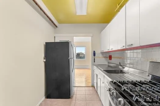 Kitchen featuring stainless steel appliances, baseboard heating, tasteful backsplash, white cabinetry, and light tile patterned flooring Kitchen featuring stainless steel appliances, baseboard heating, tasteful backsplash, white cabinetry, and light tile patterned flooring