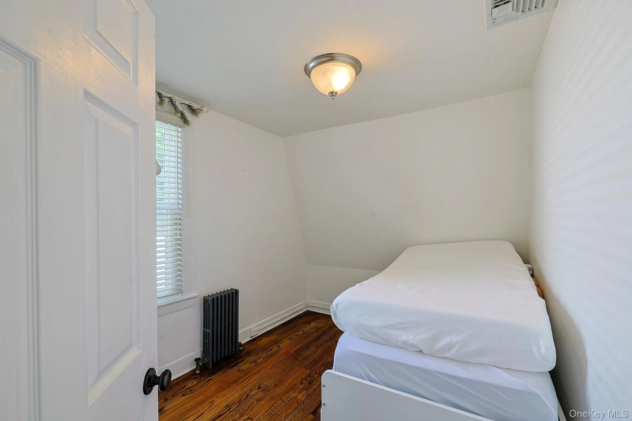 Room featuring wood-finish flooring, white painted walls, and a window with blinds Room featuring wood-finish flooring, white painted walls, and a window with blinds