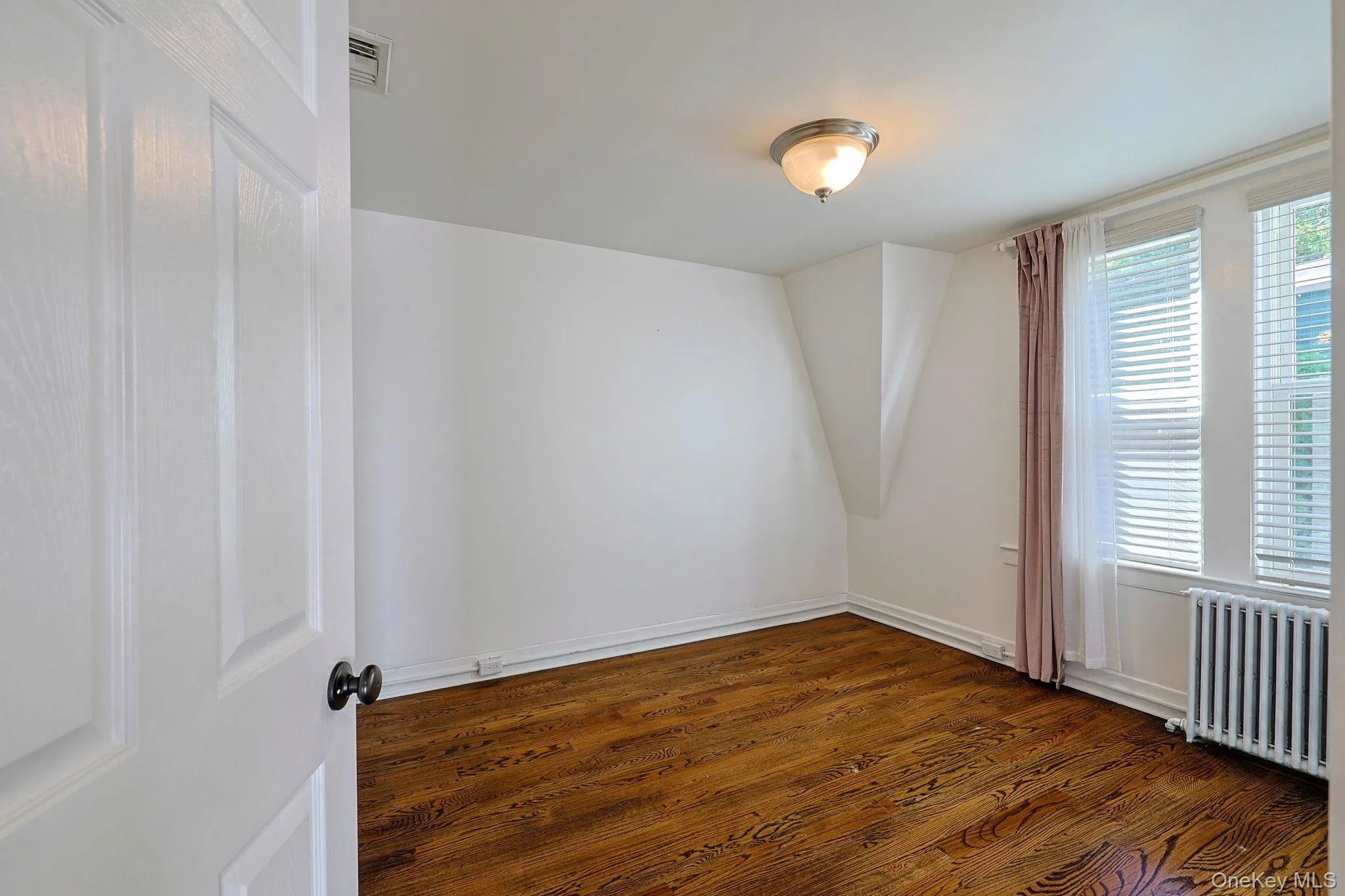 Hardwood flooring featuring a natural wood grain, white baseboards, and a semi-flush mount ceiling light Hardwood flooring featuring a natural wood grain, white baseboards, and a semi-flush mount ceiling light