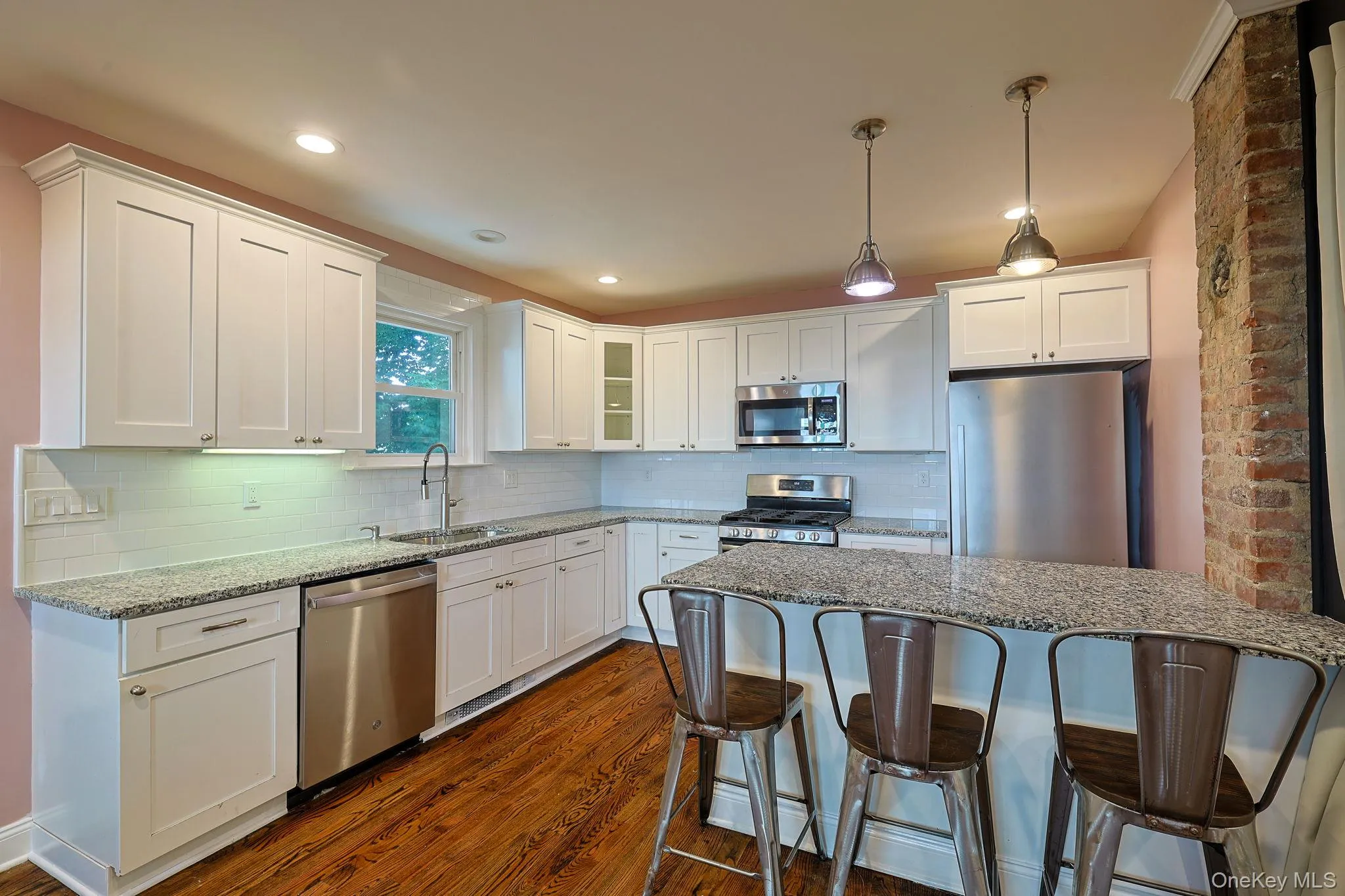 Kitchen featuring white shaker-style cabinetry, stainless steel appliances, granite countertops, wood-finish flooring, and a subway tile backsplash Kitchen featuring white shaker-style cabinetry, stainless steel appliances, granite countertops, wood-finish flooring, and a subway tile backsplash