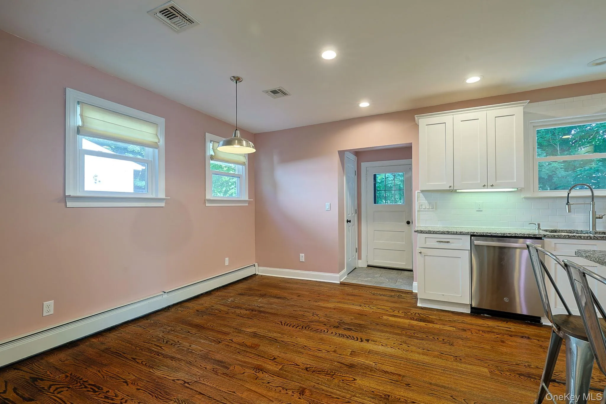 Kitchen and dining area featuring wood-finish flooring, white shaker cabinetry, stainless steel appliances, and a tiled backsplash Kitchen and dining area featuring wood-finish flooring, white shaker cabinetry, stainless steel appliances, and a tiled backsplash