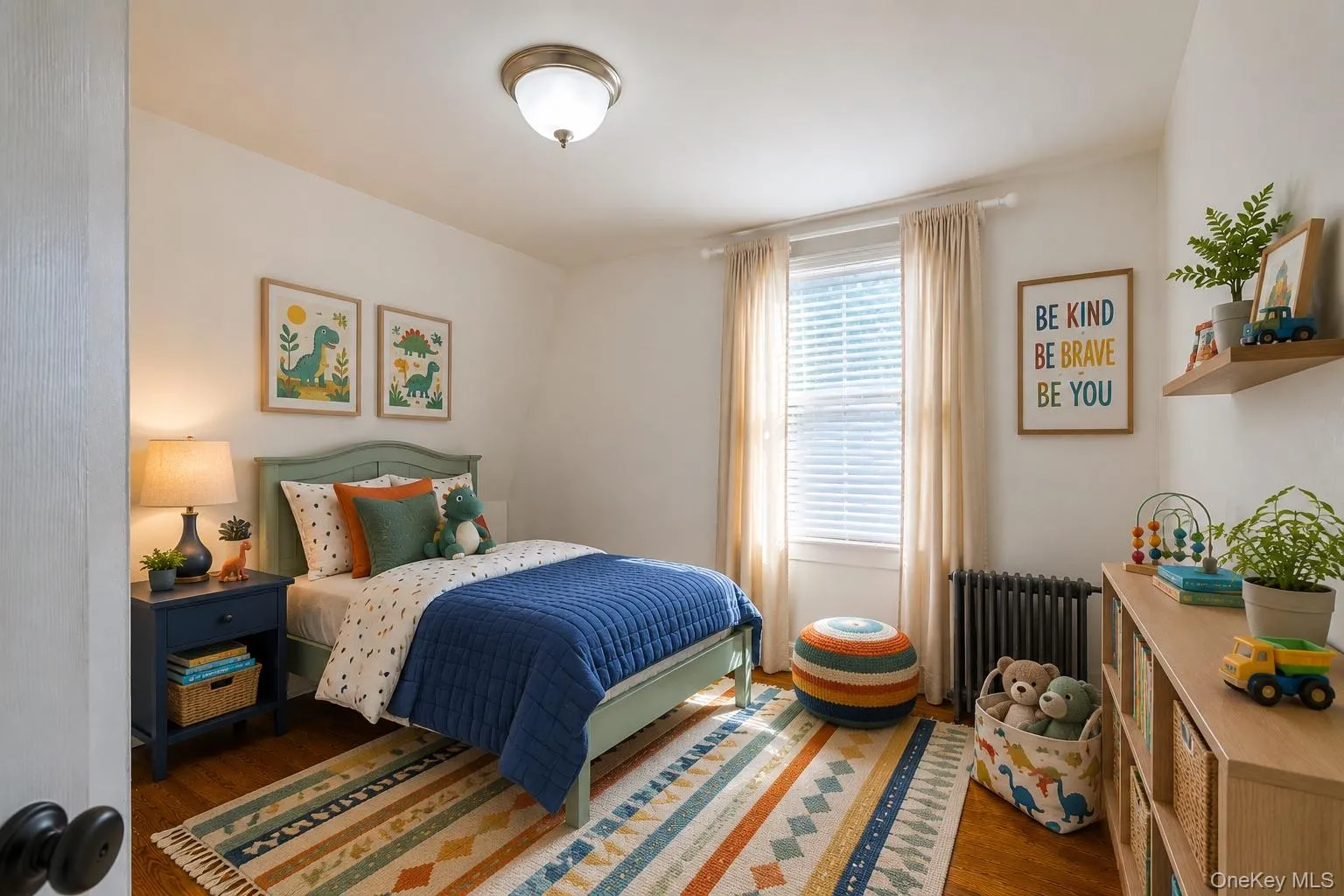 Virtually-staged kids' bedroom featuring wood-finish flooring, a single window with blinds, and a built-in radiator Virtually-staged kids' bedroom featuring wood-finish flooring, a single window with blinds, and a built-in radiator