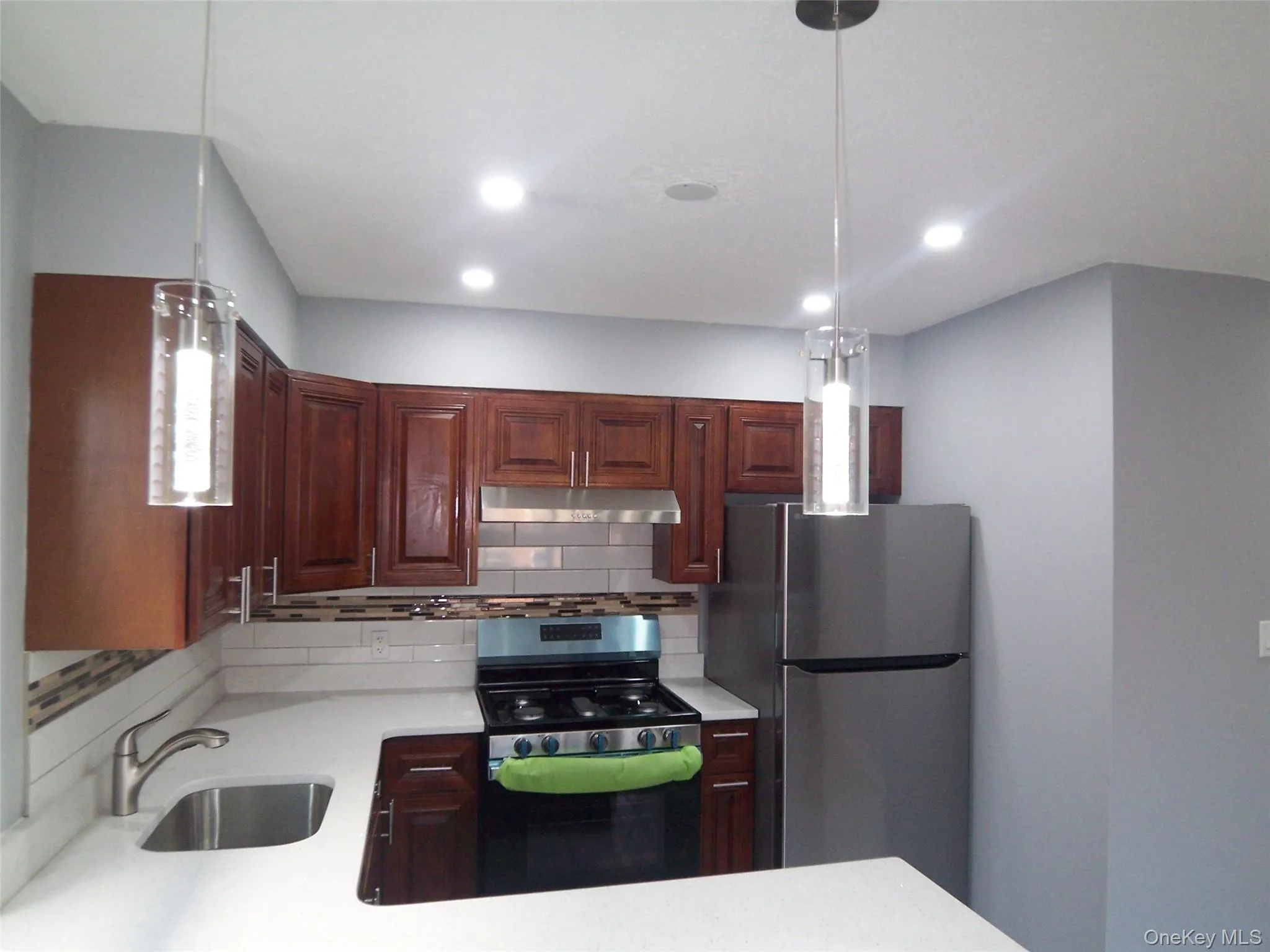 Contemporary kitchen featuring dark wood cabinetry, light-toned countertops, and a subway tile backsplash Contemporary kitchen featuring dark wood cabinetry, light-toned countertops, and a subway tile backsplash