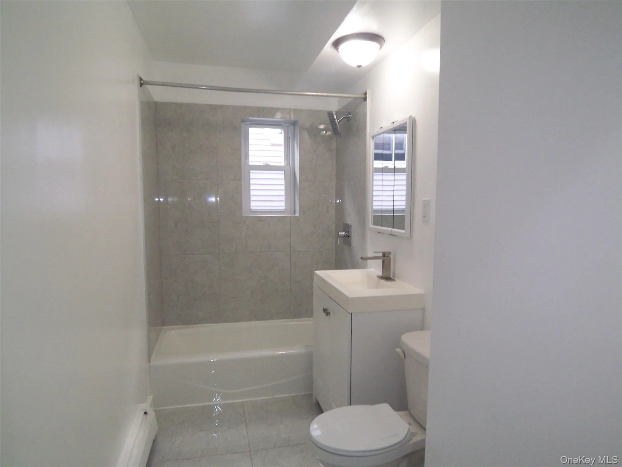 Bathroom featuring a built-in tub with a shower fixture, light-toned wall tiling, white vanity with an integrated sink, polished chrome faucet, and a wall-mounted medicine cabinet Bathroom featuring a built-in tub with a shower fixture, light-toned wall tiling, white vanity with an integrated sink, polished chrome faucet, and a wall-mounted medicine cabinet