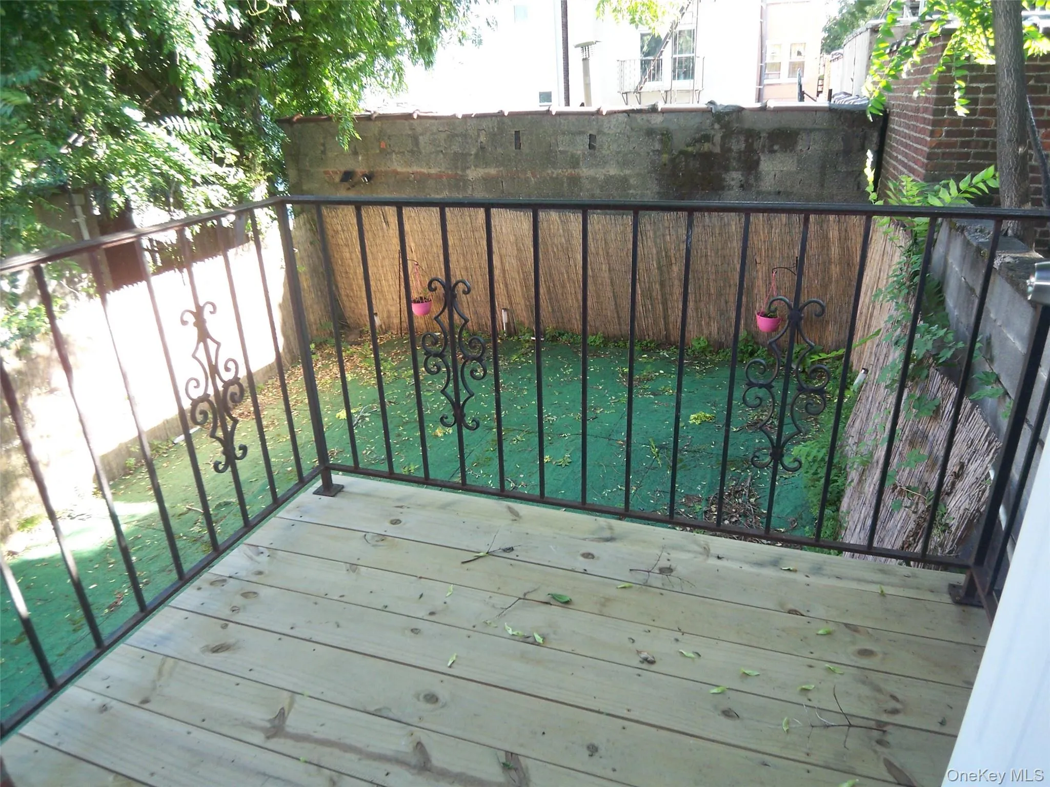 Outdoor wood deck with black wrought iron railing featuring ornate scrollwork, overlooking a compact yard with green ground covering and a concrete retaining wall Outdoor wood deck with black wrought iron railing featuring ornate scrollwork, overlooking a compact yard with green ground covering and a concrete retaining wall