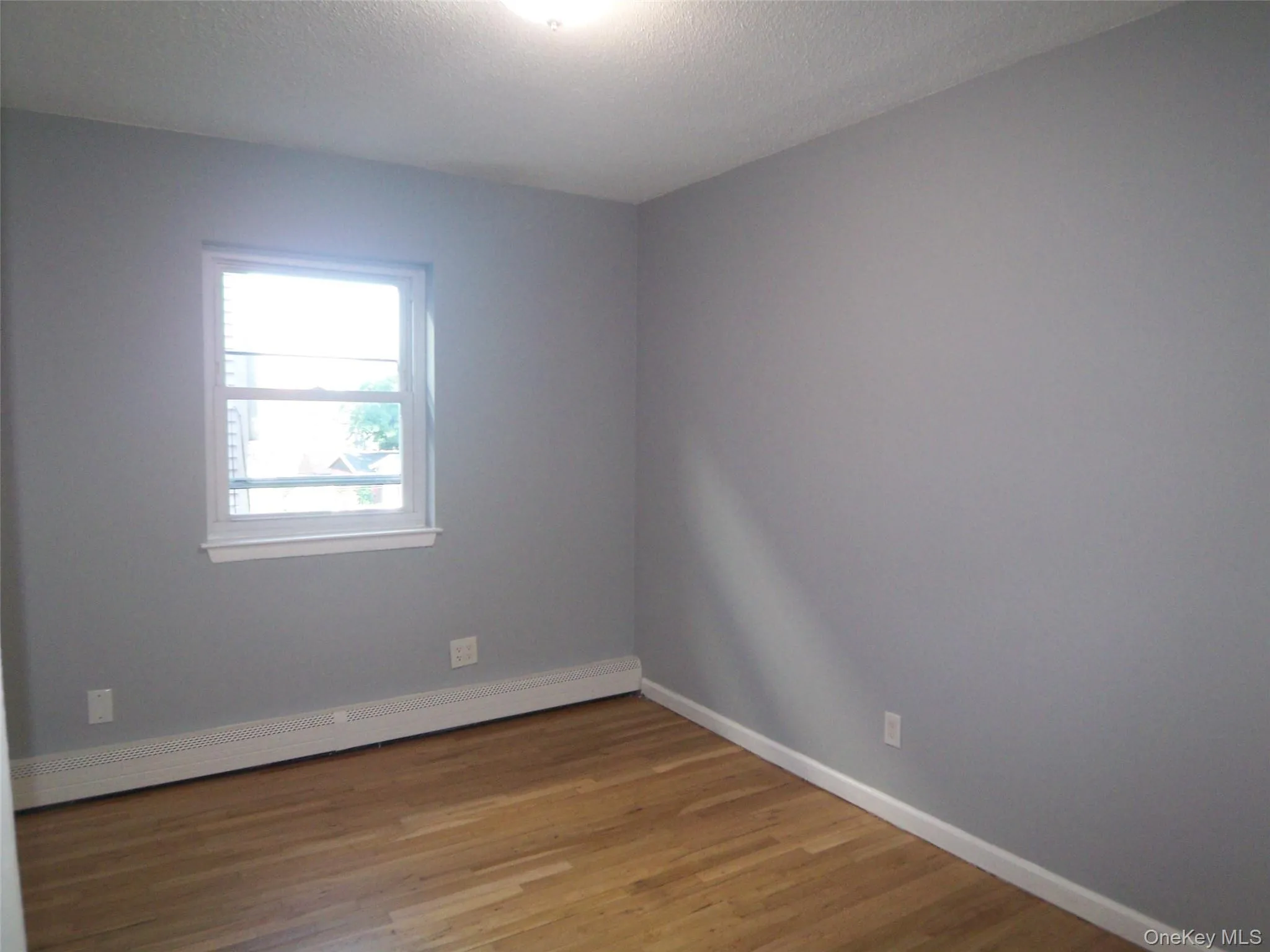 Neutral-toned walls complement wood-finish flooring in this room featuring a window with white trim Neutral-toned walls complement wood-finish flooring in this room featuring a window with white trim