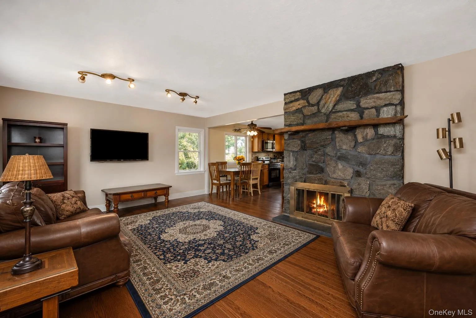 Living area featuring a stone fireplace with a wood mantle, wood-finish flooring, and recessed ceiling lighting Living area featuring a stone fireplace with a wood mantle, wood-finish flooring, and recessed ceiling lighting