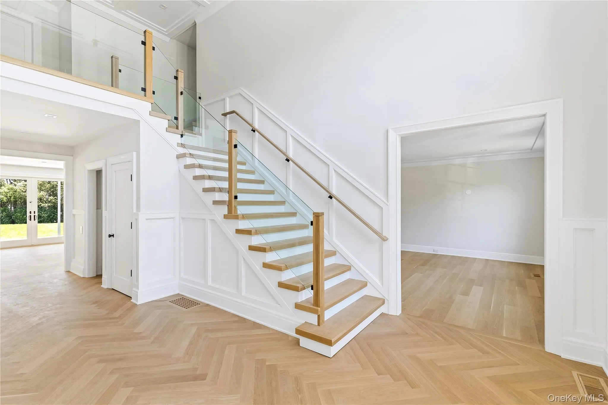 A dramatic two-story foyer welcomes guests with herringbone hardwood floors and a striking modern staircase with contemporary glass railings. A dramatic two-story foyer welcomes guests with herringbone hardwood floors and a striking modern staircase with contemporary glass railings.